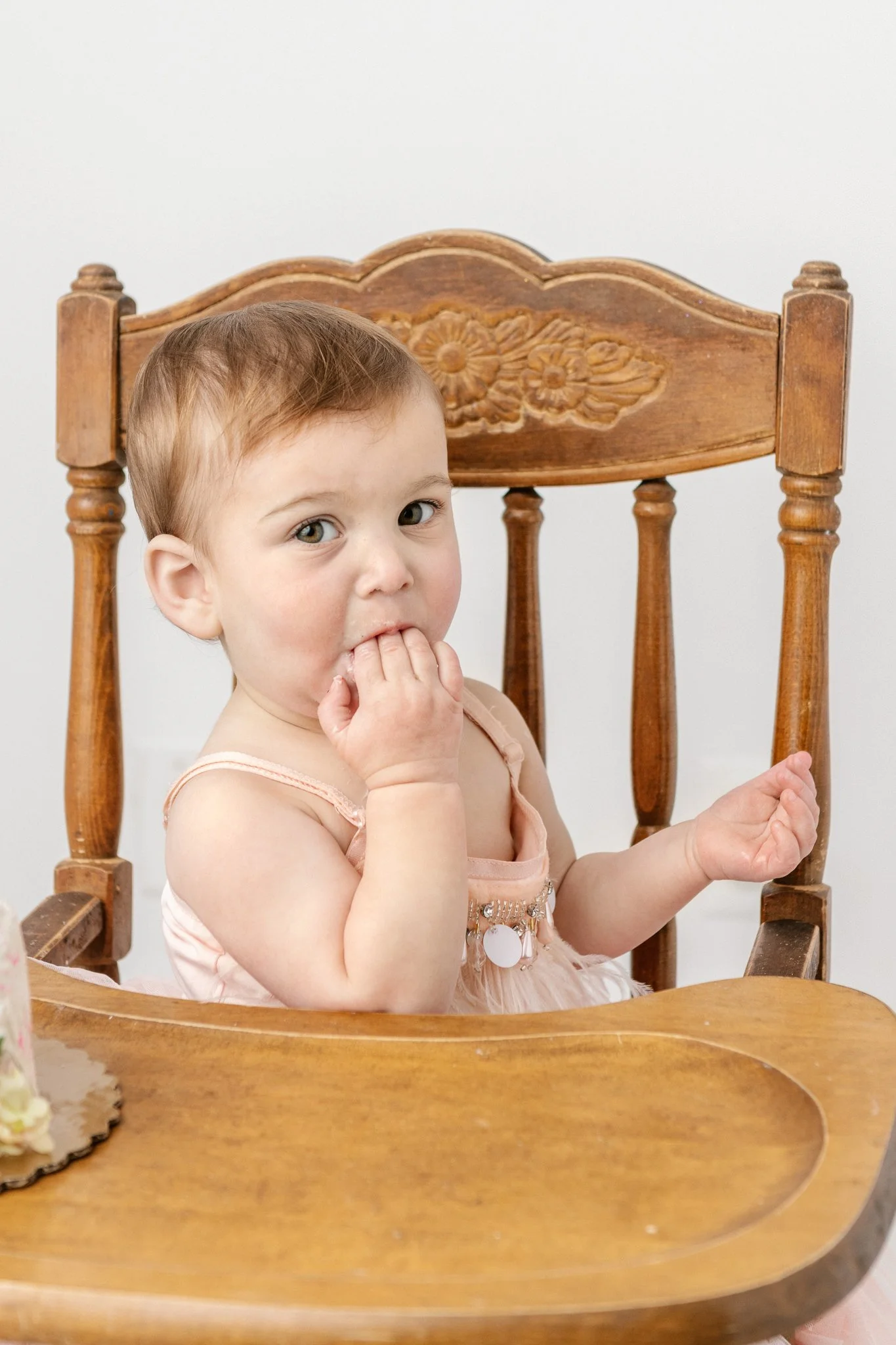  A baby girl sits in an antique high-chair and eats her cake by Nicole Hawkins Photography. high chair cake smash antique high chair  first birthday portraits #NicoleHawkinsPhotography #NicoleHawkinsBabies&amp;Children #FirstBirthdayPhotography #Stud