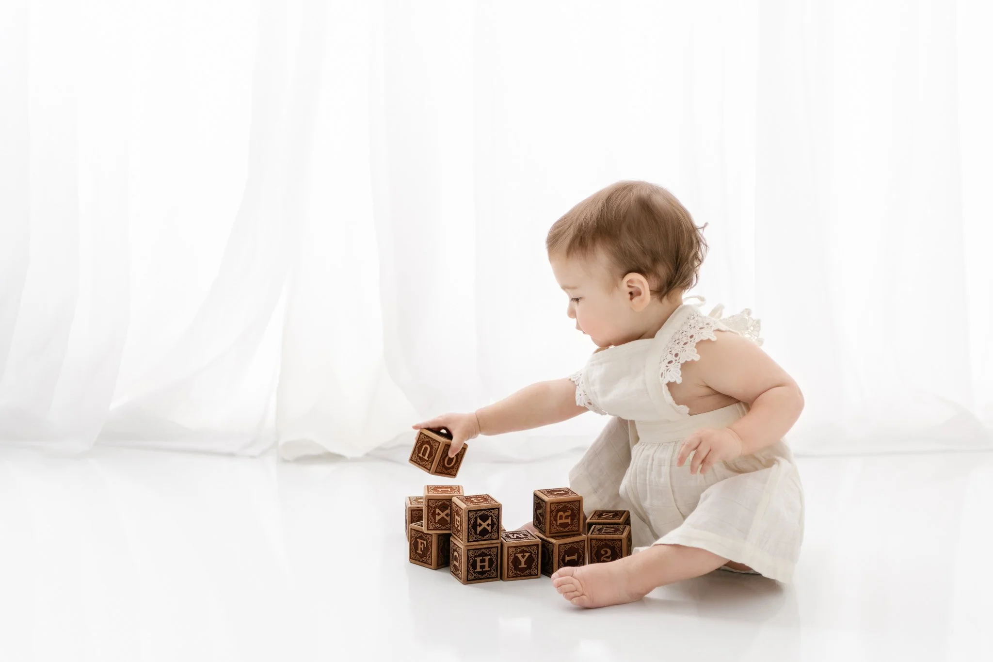  A little girl stacks wooden blocks in a white studio wearing a vintage dress by Nicole Hawkins Photography. vintage style girl dress vintage style first birthday photography #NicoleHawkinsPhotography #NicoleHawkinsBabies&amp;Children #FirstBirthdayP