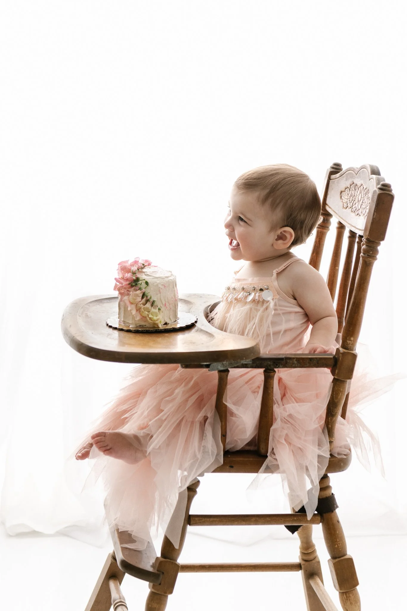  Side view of a toddler girl in a pink tutu dress sitting in a high chair with her smash cake by Nicole Hawkins Photography. smash cake vintage high chair tiny smash cake #NicoleHawkinsPhotography #NicoleHawkinsBabies&amp;Children #FirstBirthdayPhoto