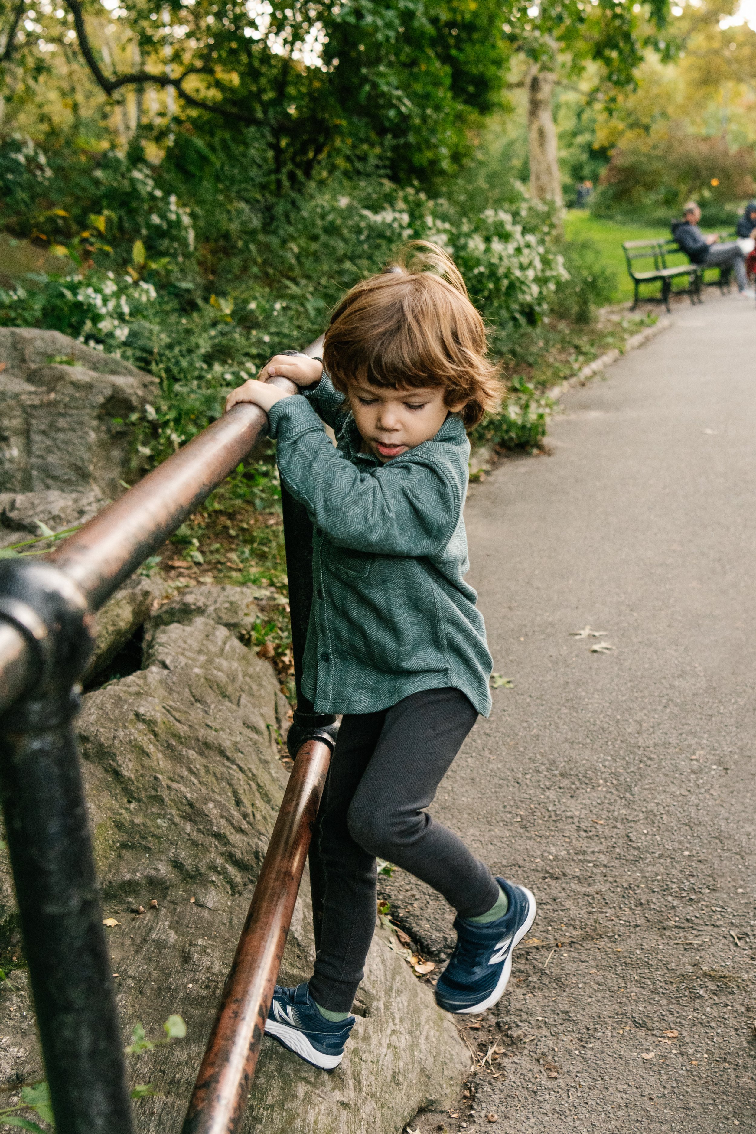  A little boy plays on a railing in Central Park during a family session with Nicole Hawkins PHotography. boy in central park playing child portrait #NicoleHawkinsPhotography #NicoleHawkinsFamilies #NJphotographers #familyphotos #CentralParkPhotograp