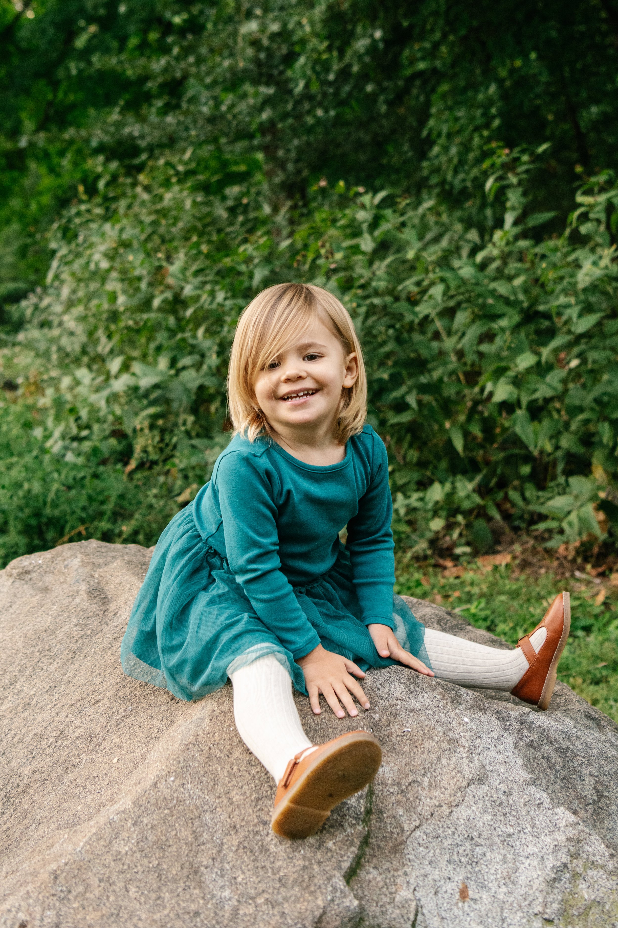  A little girl sits on a rock and smiles in Central Park by Nicole Hawkins Photography. sitting on a rock exploring girl Central Park #NicoleHawkinsPhotography #NicoleHawkinsFamilies #NJphotographers #familyphotos #CentralParkPhotography #CentralPark
