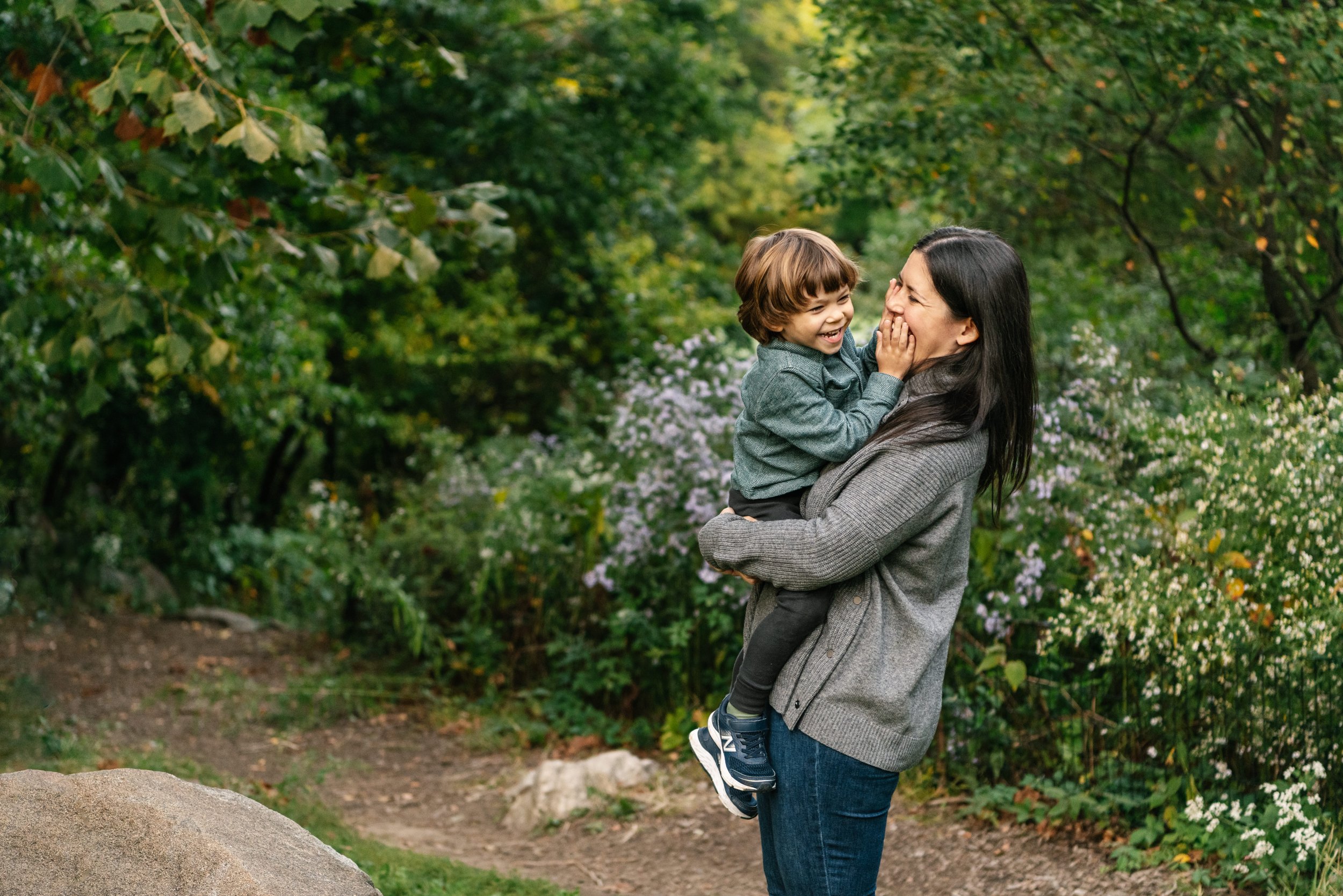  New York Central Park family portraits featuring a mother in casual attire holding her little boy with brown hair by Nicole Hawkins Photography. casual family pictures green background #NicoleHawkinsPhotography #NicoleHawkinsFamilies #NJphotographer