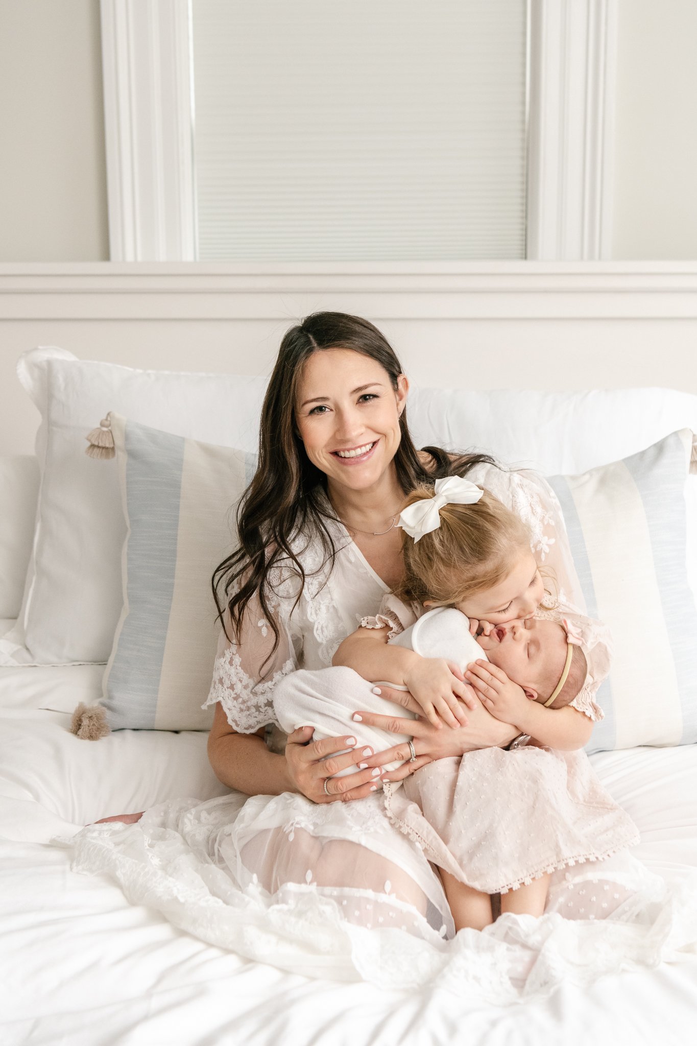  A mother sits on her bed with her two little girls in Chatham, MA by Nicole Hawkins Photography. sitting on bed pose bright and crisp style newborns #NicoleHawkinsPhotography #NicoleHawkinsNewborns #Babygirl #Newbornfamilyportraits #ChathamNewbornPh