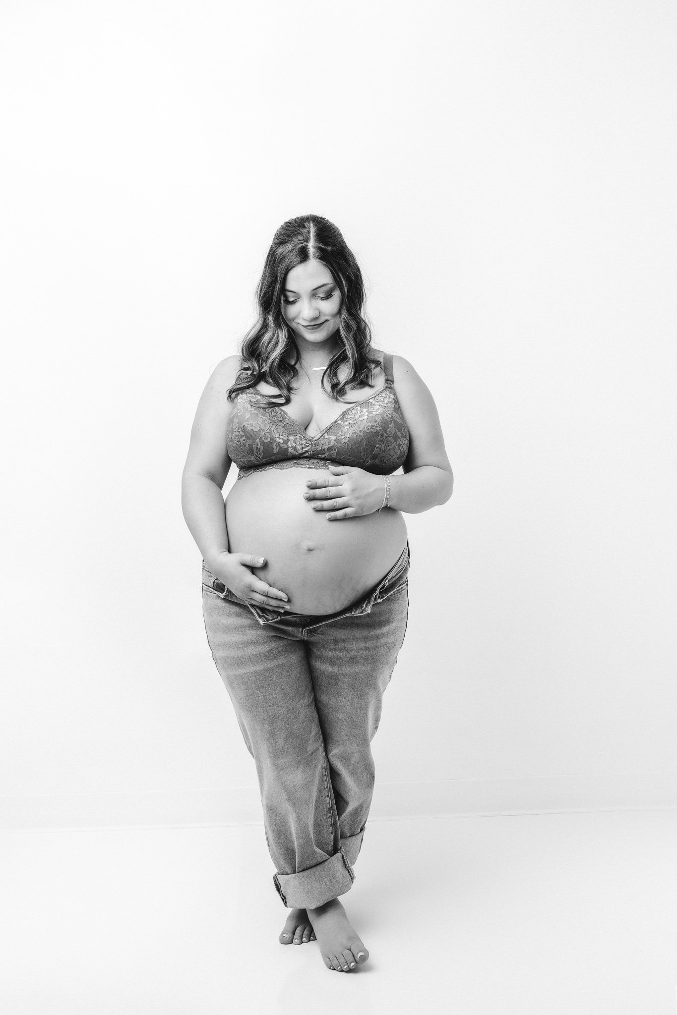  In a white studio in NJ Nicole Hawkins photography captures a portrait of a mother holding her baby bump. white studio jean and bra maternity portrait #NicoleHawkinsPhotography #NicoleHawkinsMaternity #Babyontheway #studiomaternityNJ #whitestudiomat