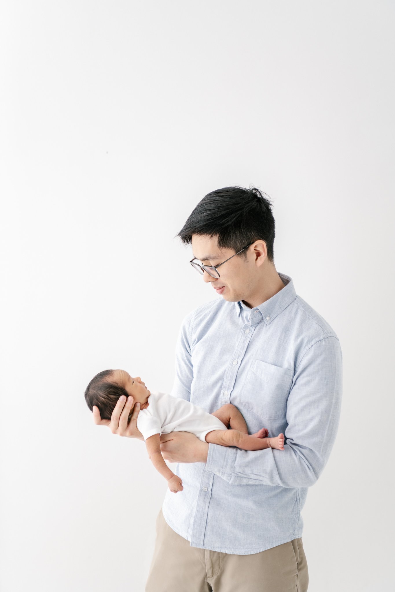  In a white studio in NJ Nicole Hawkins Photography captures a father holding his newborn baby boy in his hands. father and newborn Asian newborns #NicoleHawkinsPhotography #NicoleHawkinsNewborns #Babyboy #studionewbornsNJ #studionewbonportraits #NYn