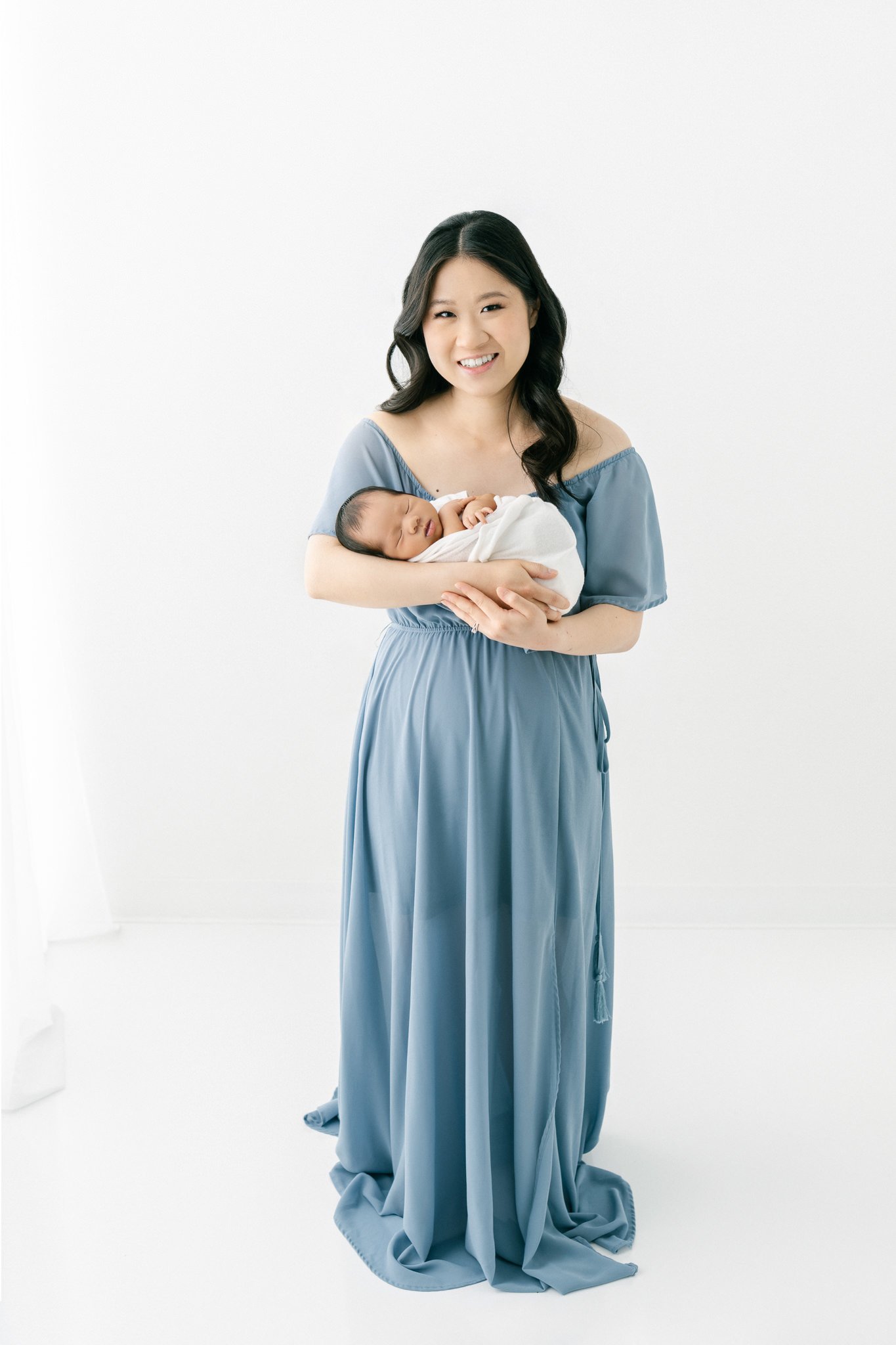  A mother in a blue gown holds her sleeping newborn baby boy by Nicole Hawkins Phtoography in New Jersey. New Jersey Newborn Photography #NicoleHawkinsPhotography #NicoleHawkinsNewborns #Babyboy #studionewbornsNJ #studionewbonportraits #NYnewbornphot