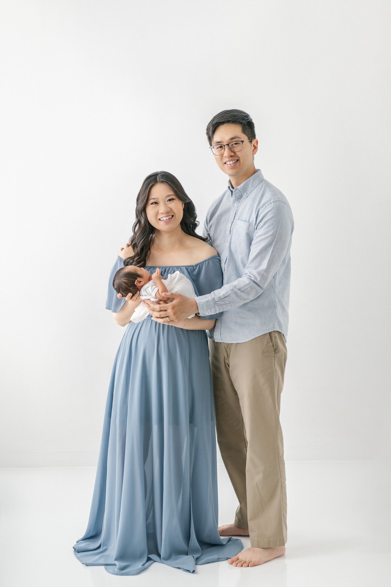  A family of three portrait with light blue clothing at a white studio near New York by Nicole Hawkins Photography. light blue studio outfits #NicoleHawkinsPhotography #NicoleHawkinsNewborns #Babyboy #studionewbornsNJ #studionewbonportraits #NYnewbor