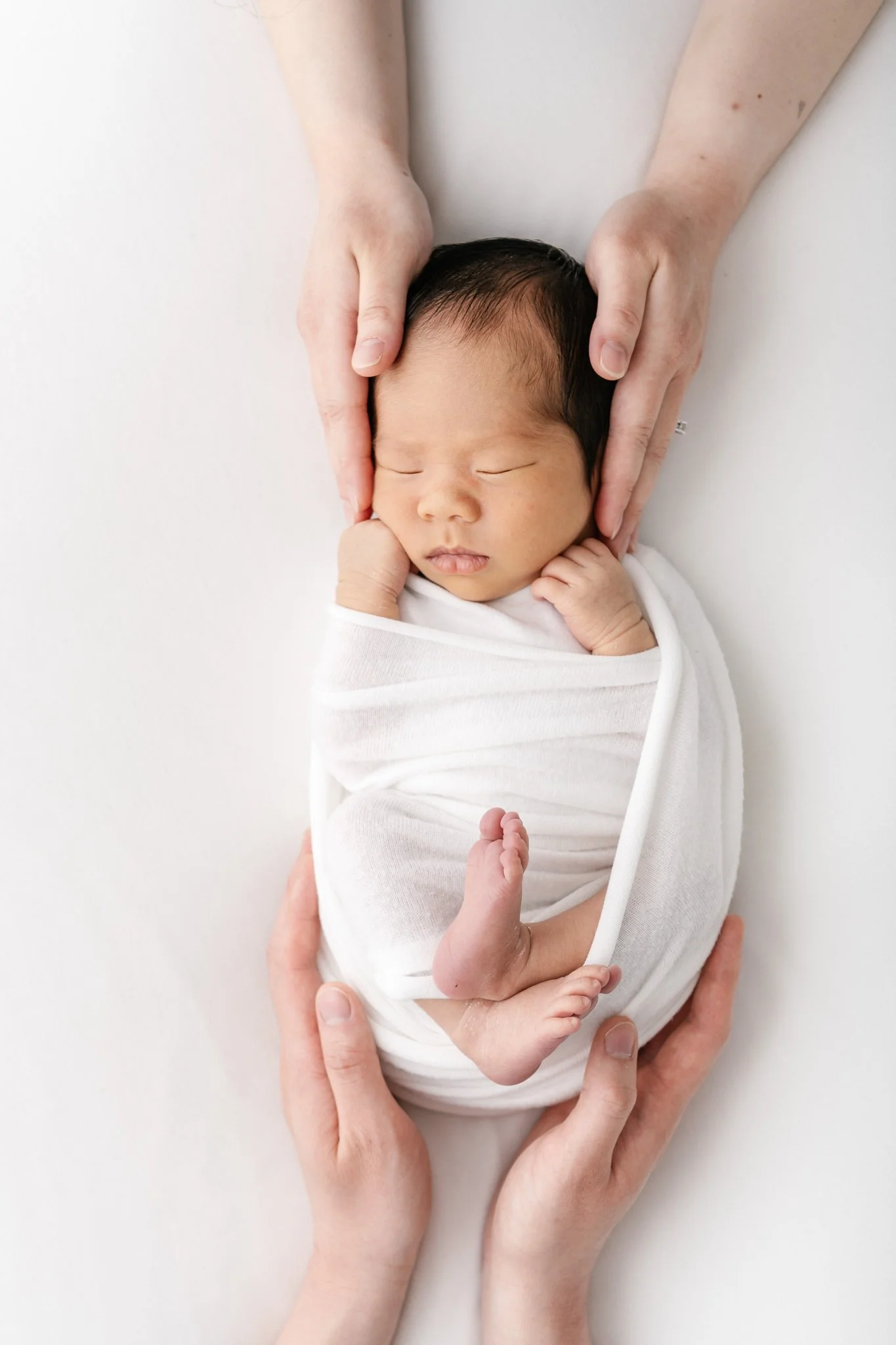  A baby boy swaddled and sleeping is comforted by his parents touch by Nicole Hawkins Photography. parent's holding baby together #NicoleHawkinsPhotography #NicoleHawkinsNewborns #Babyboy #studionewbornsNJ #studionewbonportraits #NYnewbornphotographe