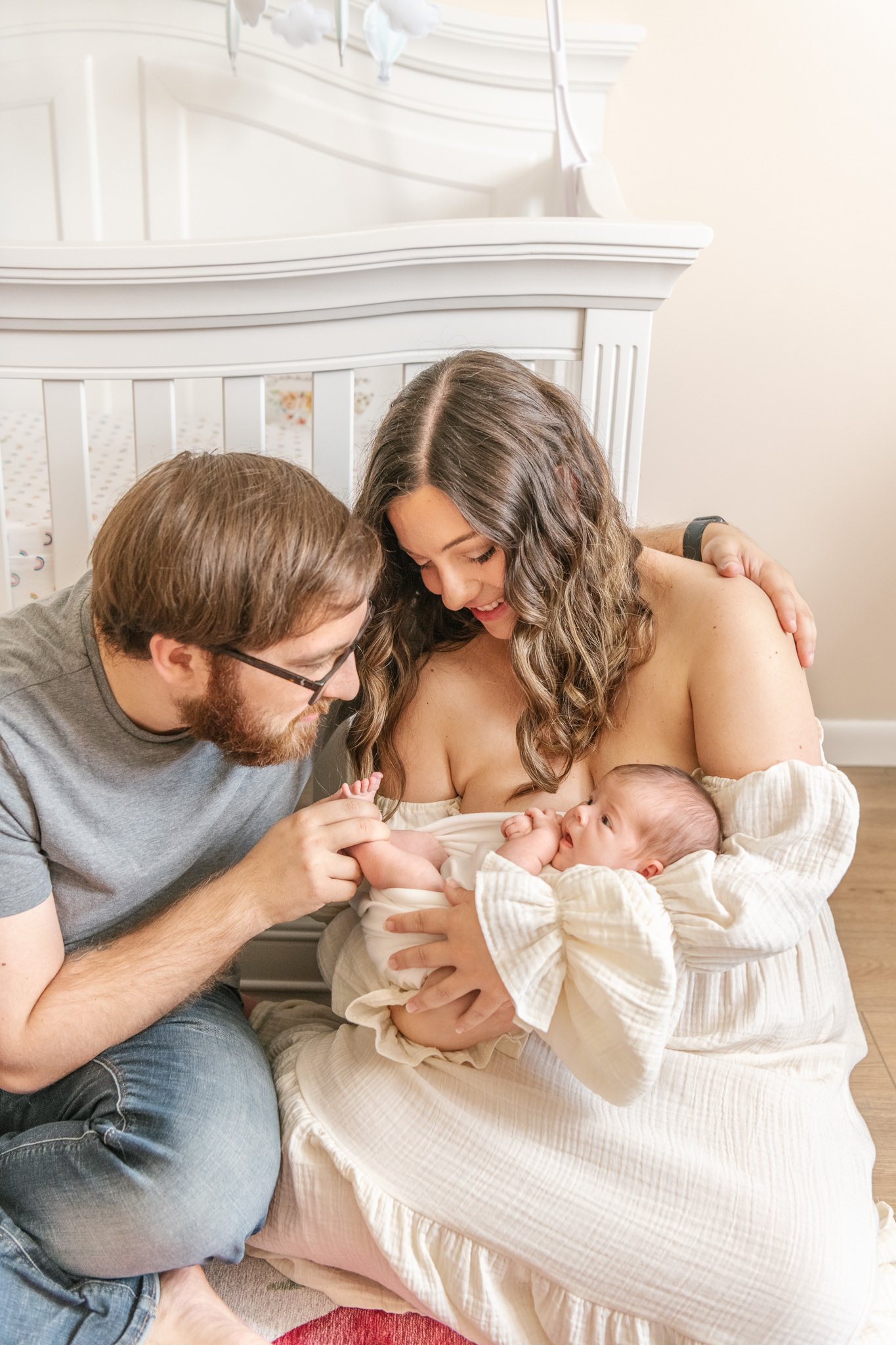  A father and mother play with a newborn's toes while sitting next to the crib by Nicole Hawkins Photography. father and mother and baby in home newborns #NicoleHawkinsPhotography #NicoleHawkinsNewborns #Babygirl #inhomenewbornsNJ #homenewbonportrait