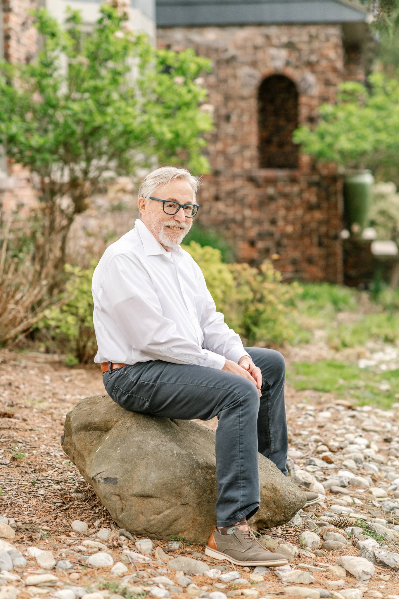  East Coast family photographer Nicole Hawkins photography captures a grandpa sitting on a rock in a beautifully landscaped yard. grandfather portrait #NicoleHawkinsPhotography #NicoleHawkinsfamilies #AtHomePortraits #EastCoastFamilyPhotographer #New