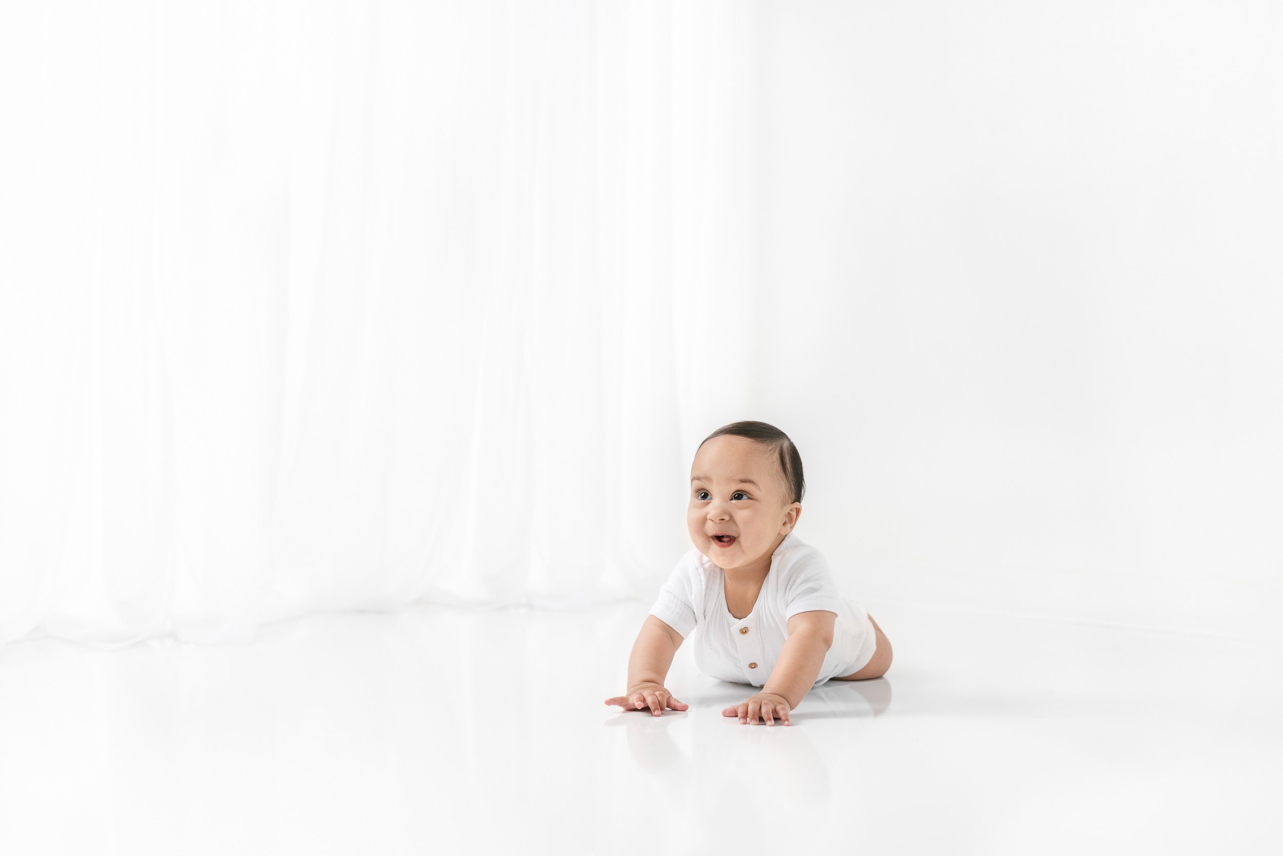  A little boy smiles as he crawls around a white studio in New Jersey by Nicole Hawkins Photography. professional studio photographer NJ/NY area #NicoleHawkinsPhotography #NicolewHawkinsNewborns #NewJerseyNewborns #NewJerseyStudioNewborns #StudioNewb