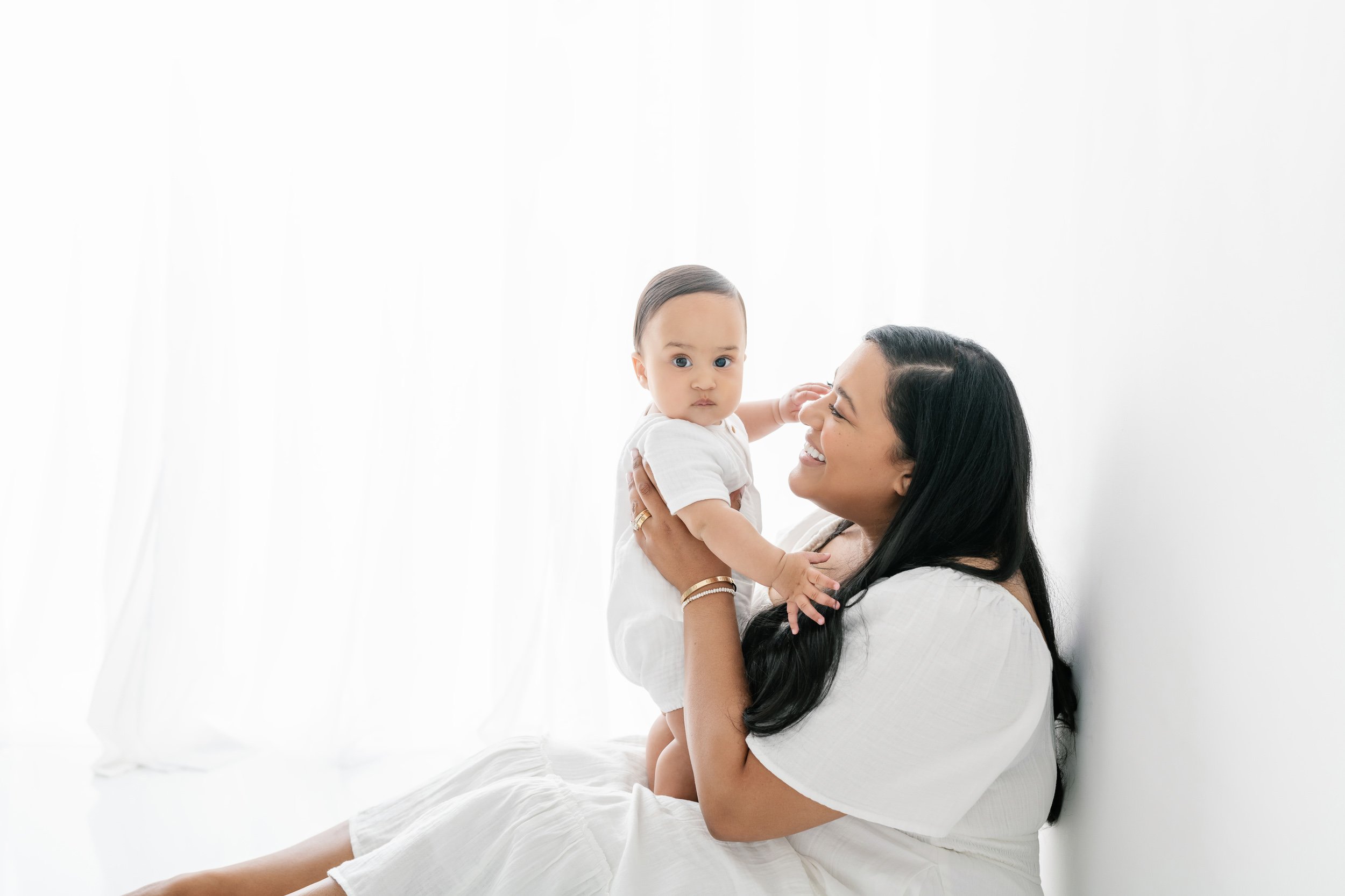  Nicole Hawkins's Photography captures a baby boy with big eyes playing with his mother. Mother style white dress for studio portraits black hair baby #NicoleHawkinsPhotography #NicolewHawkinsNewborns #NewJerseyNewborns #NewJerseyStudioNewborns #Stud