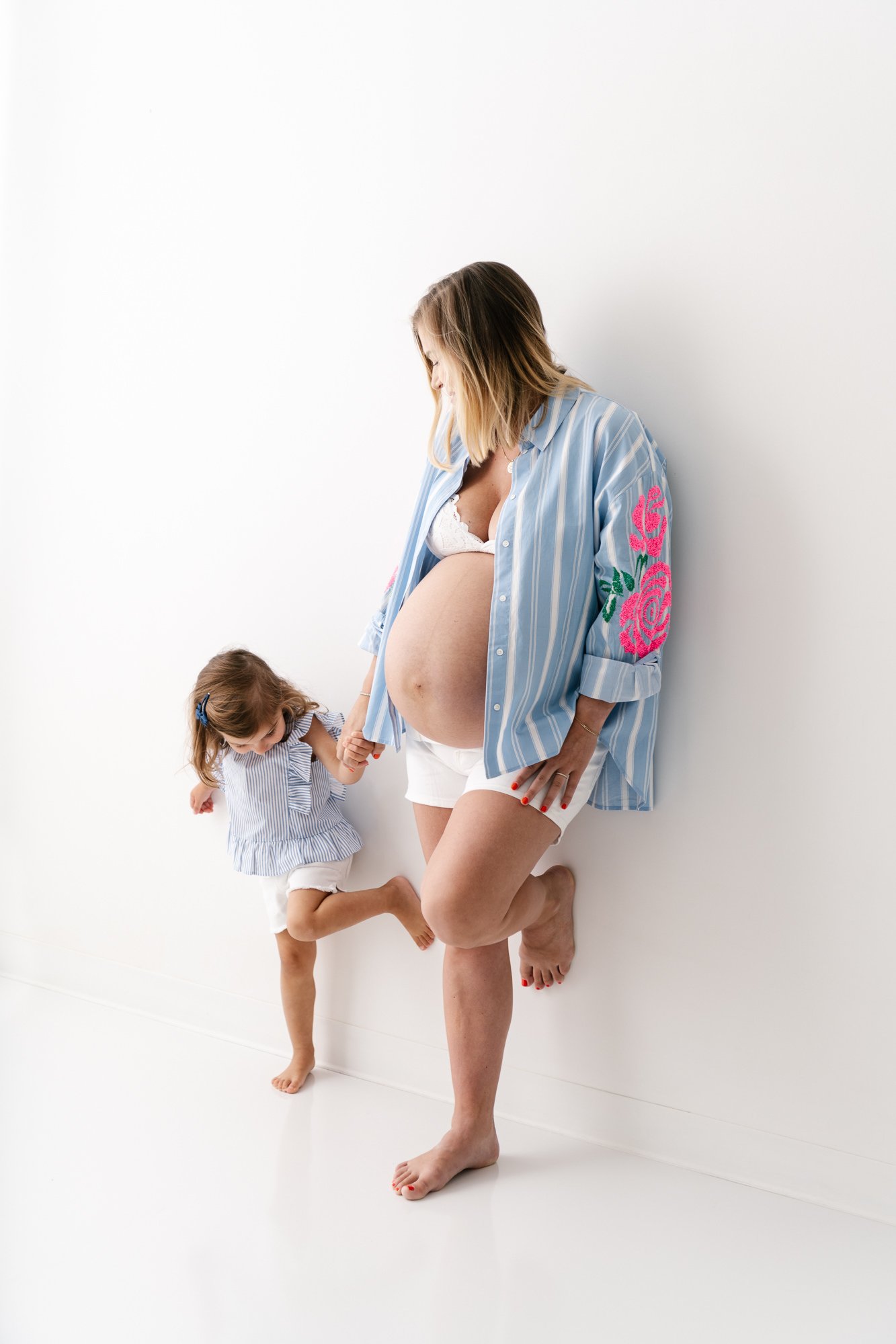  New Jersey maternity photographer Nicole Hawkins Photography captures a pregnant mother and daughter standing together playing against a wall. mother portrait baby on the way pregnancy bump portrait #NicoleHawkinsPhotography #NicoleHawkinsMaternity 
