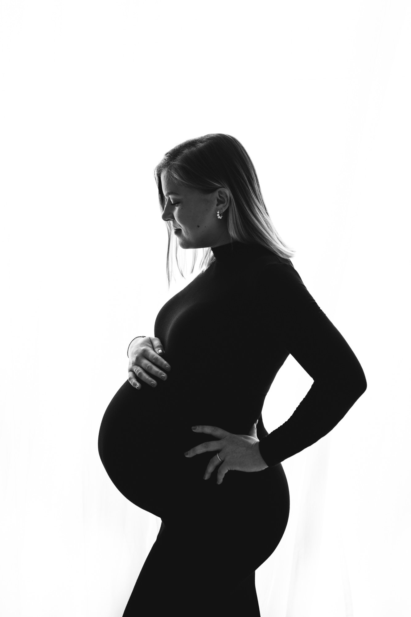  Maternity silhouette portrait with a mother holding her baby bump at a white studio in NJ by Nicole Hawkins Photography. timeless maternity portrait studio silhouette portraits #NicoleHawkinsPhotography #NicoleHawkinsMaternity #MaternityStudioPortra