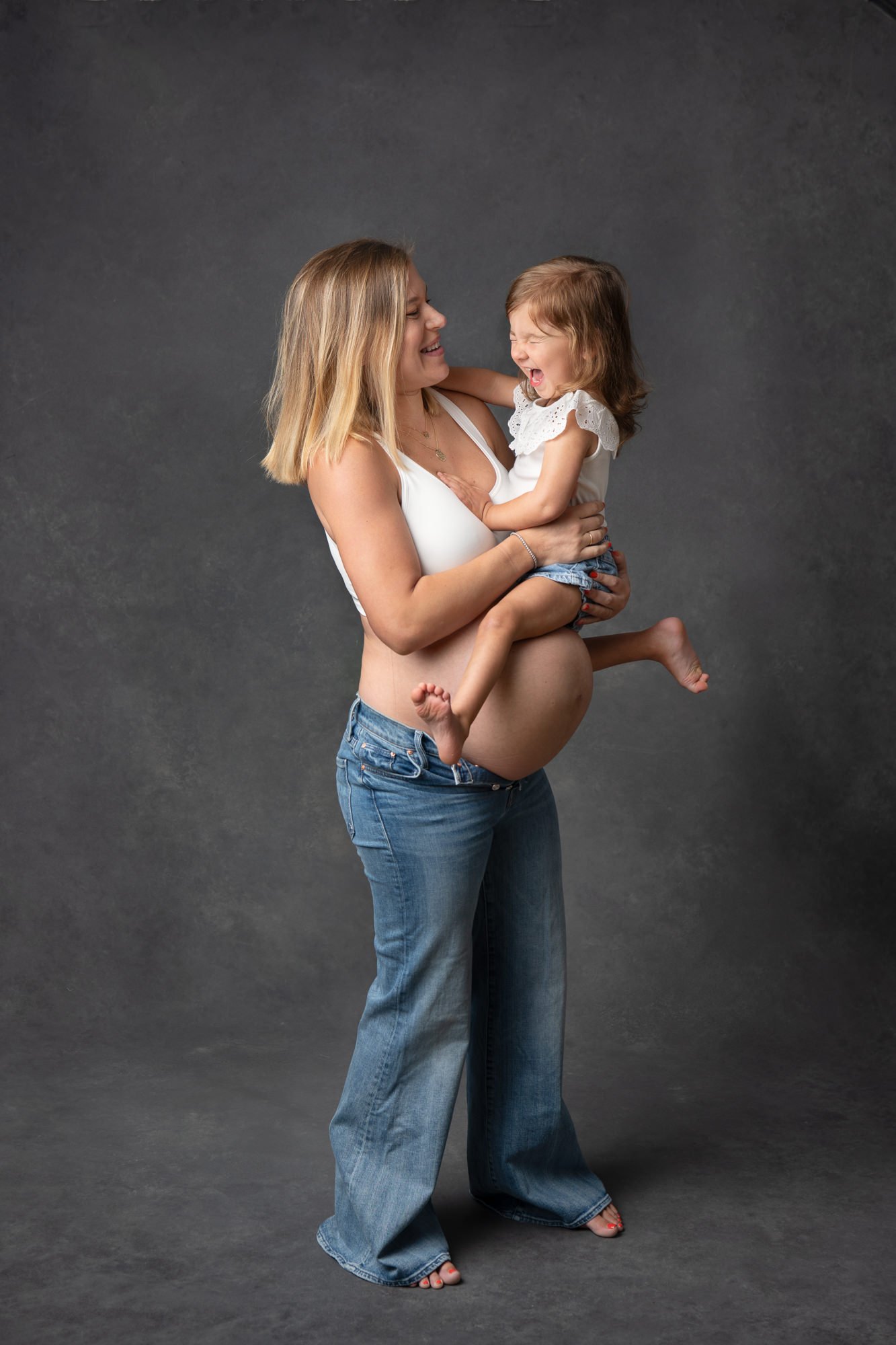  A big sister plays while sitting on her mommy's belly during a studio session in Northern NJ by Nicole Hawkins Photography. Northern NJ/ NY area maternity portraits big sister on belly #NicoleHawkinsPhotography #NicoleHawkinsMaternity #MaternityStud