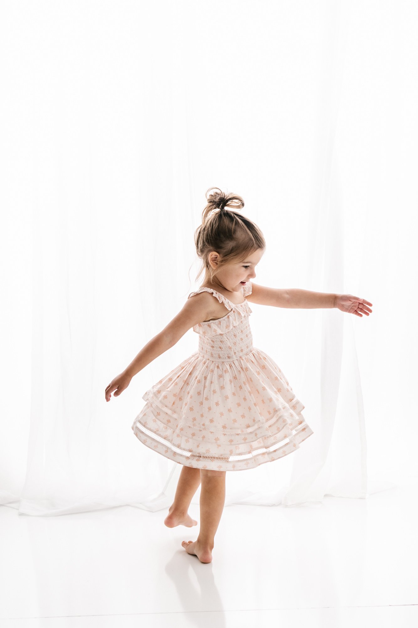  Nicole Hawkins Photography captures a little girl dancing around a white studio with a darling top knot bun. floral twirl dress dancing darling girl white studio family portraits #NicoleHawkinsPhotography #NicoleHawkinsMaternity #MaternityStudioPort