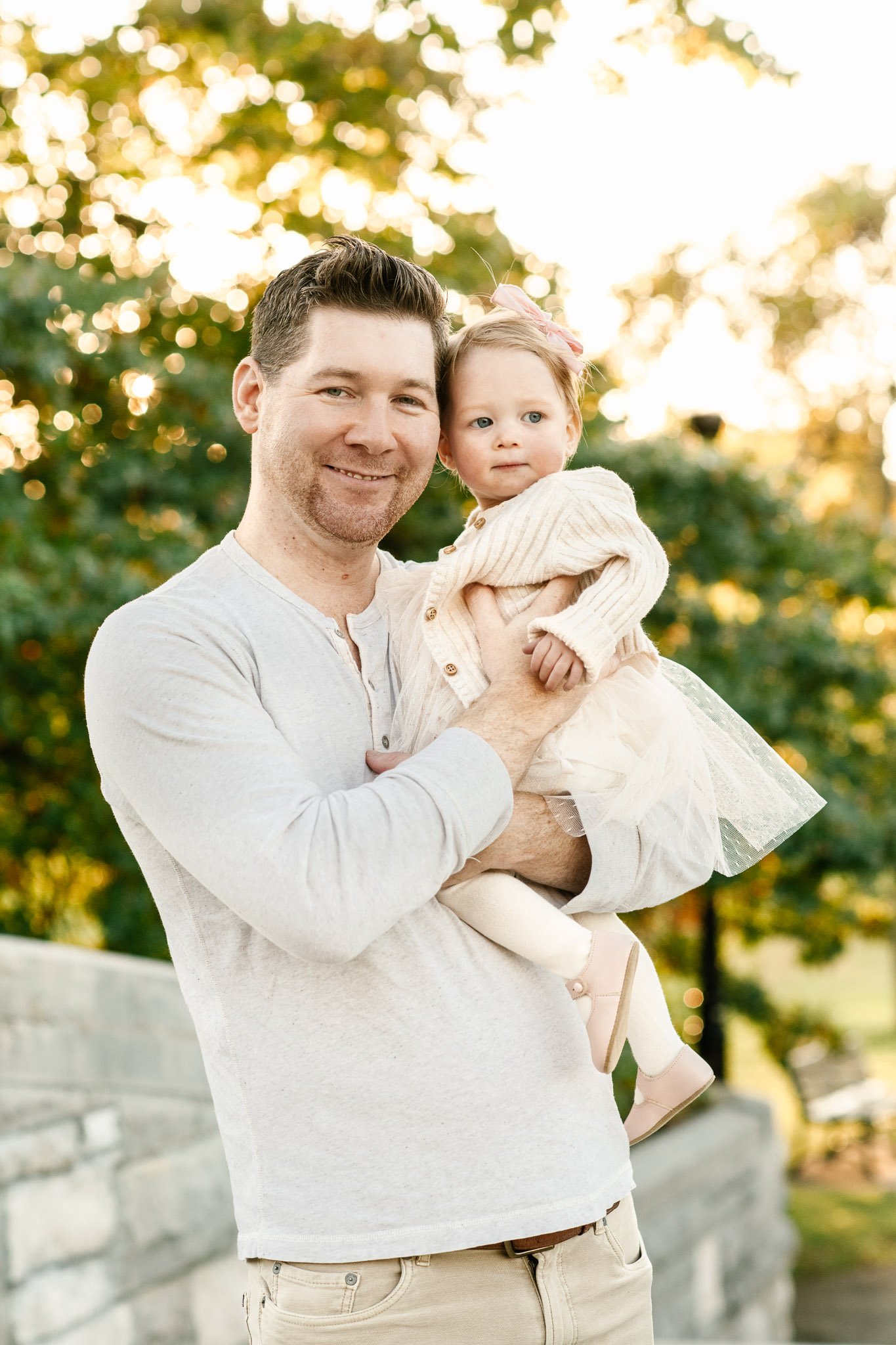  A father holds his baby girl in his arms and smiles with the fall leaves in the background by Nicole Hawkins Photography. daddy daughter little girl outfits idea for fall pics #NicoleHawkinsPhotography #NicoleHawkinsFamilies #FallFamilyPhotos #FallP