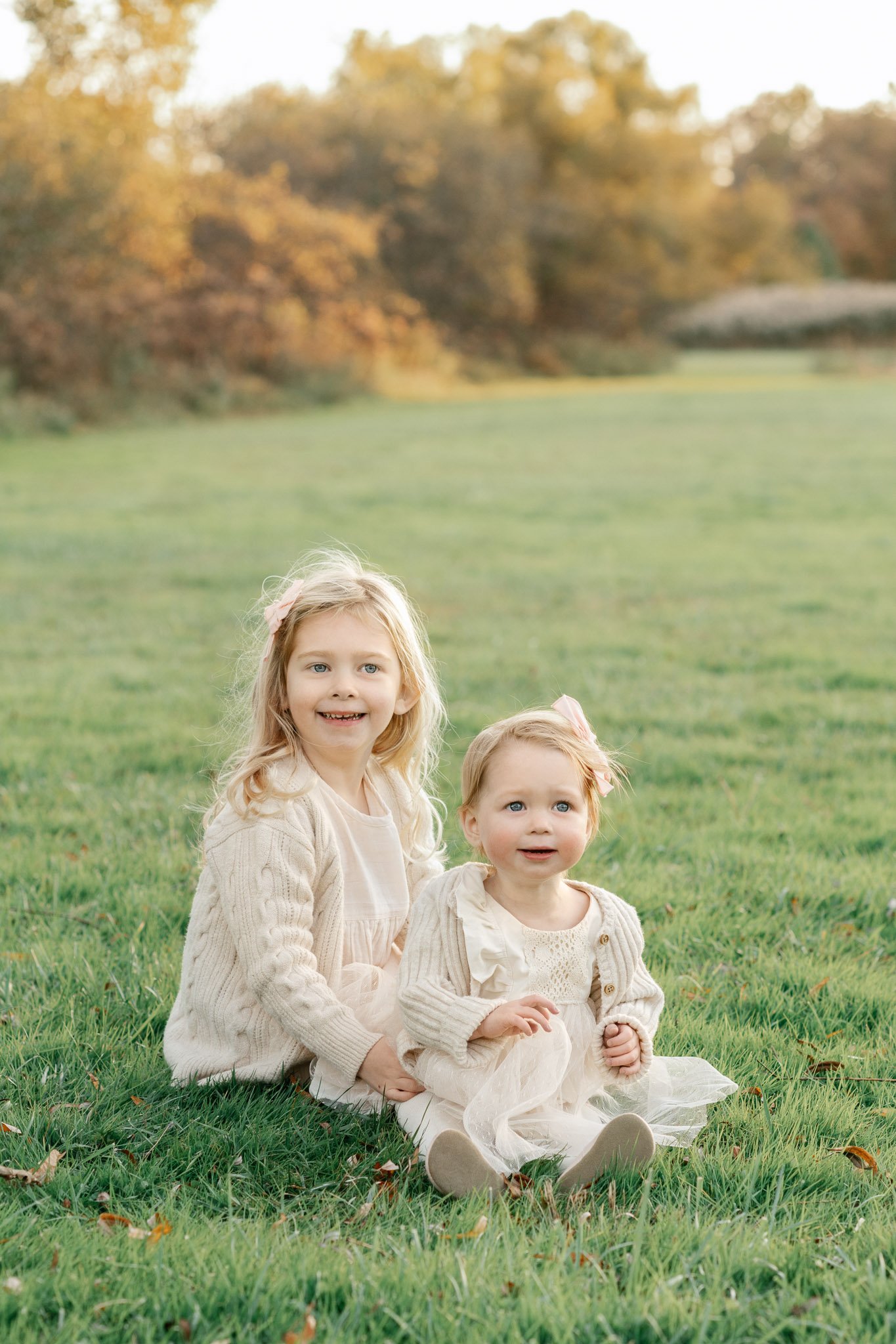  New Jersey family photographer Nicole Hawkins Photography captures two sisters in white dresses sitting on a field of grass. reasons to do fall family pics #NicoleHawkinsPhotography #NicoleHawkinsFamilies #FallFamilyPhotos #FallPortraits #NJFamilyPh