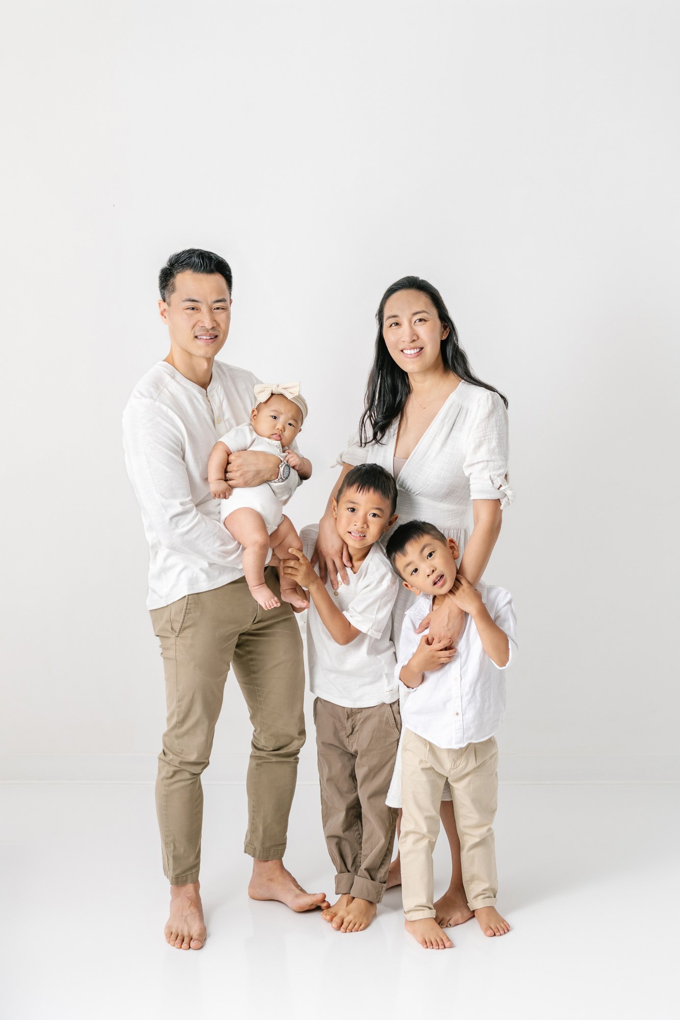    Family picture with a mom, dad, two brothers, and newborn baby sister in studio photography session by Nicole Hawkins Photography in New Jersey. Dad holds baby while mom embraces the older brothers #studionewborns #studioportraits #babystudioportr