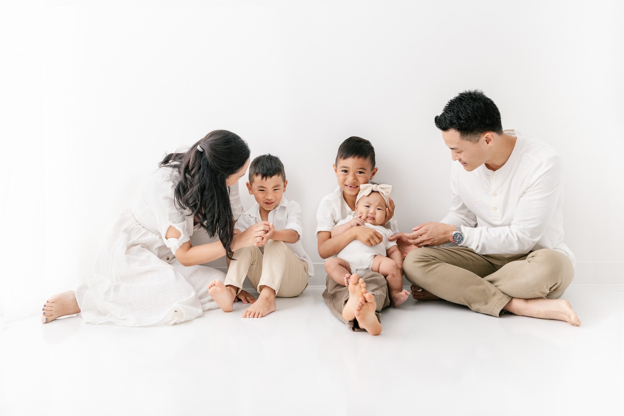    A family of five sits on the ground in family picture in New Jersey photo session. Parents look fondly at their children while kids look into the camera. Happy family picture done by Nicole Hawkins Photography #studionewborns #studioportraits #bab