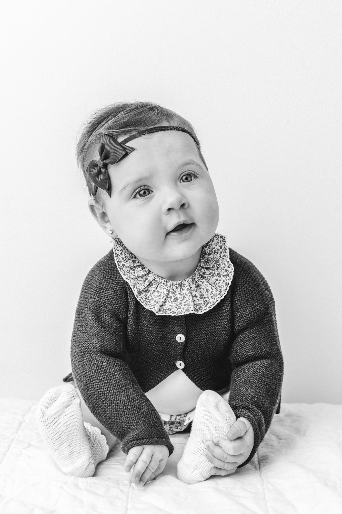  Small child sitting up in New Jersey studio during a portrait photoshoot. Picture is in black and white. Baby plays with her feet in this timeless image captured by Nicole Hawkins Photography&nbsp; #babystudioportraits #studionewborns #NewJerseyPhot