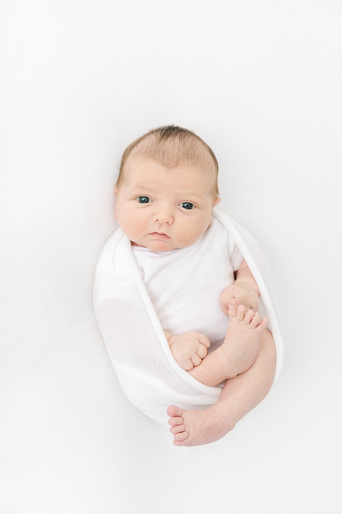  Cutest little newborn wrapped in a swaddle. Cozy newborn pictures vibes. Wide eye baby picture from above in a luxury studio session captured by Nicole Hawkins Photography in New Jersey. #newbornportraits #newbornstudioshoots #NewJerseyPhotographers