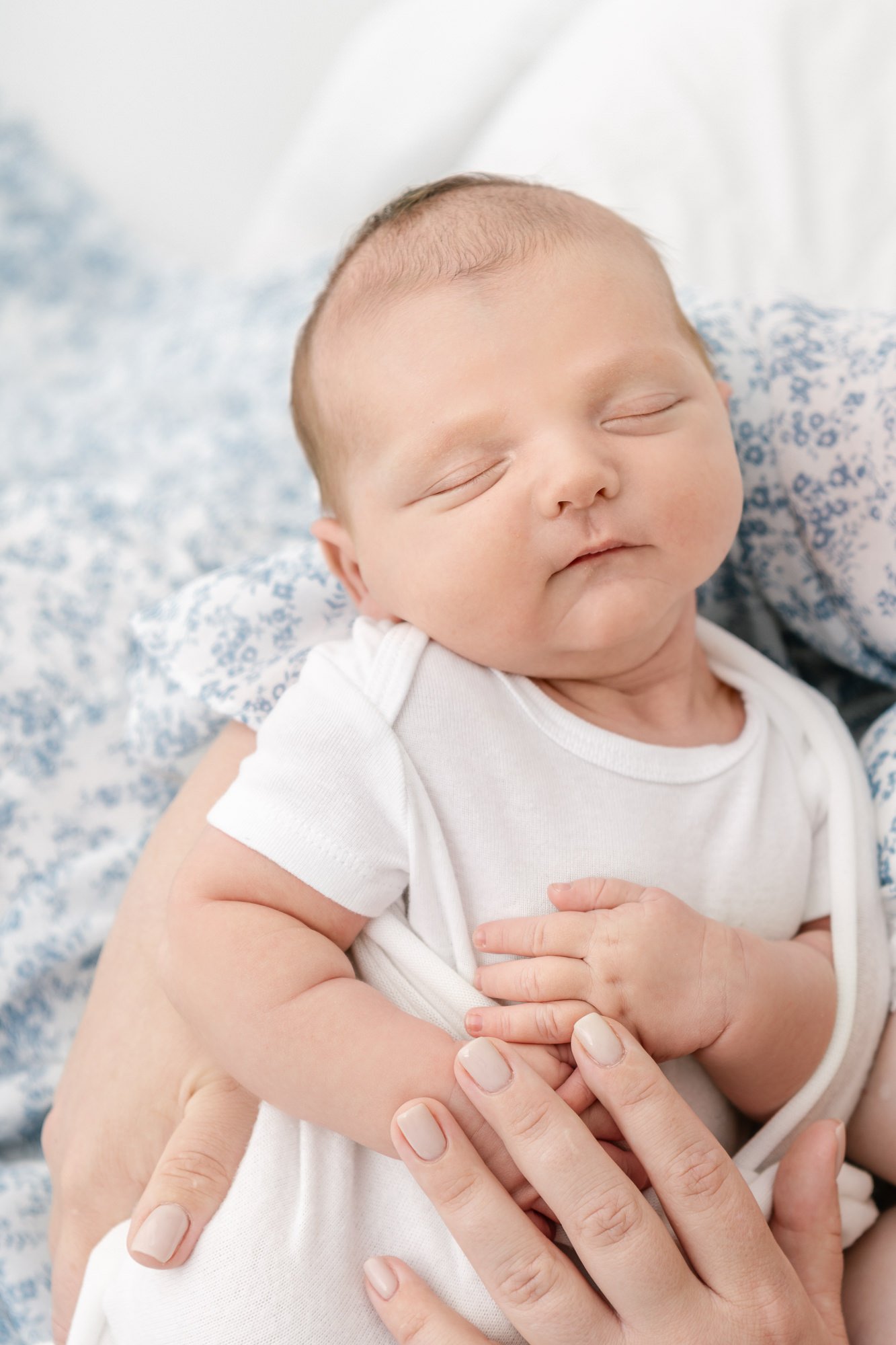    Sleeping newborn cradled in mom’s arms rests peacefully. Mom places on hand on baby’s stomach and keeps baby close to her elbow with other arm. Image captured by Nicole Hawkins Photography #newbornportraits #newbornstudioshoots #NewJerseyPhotograp