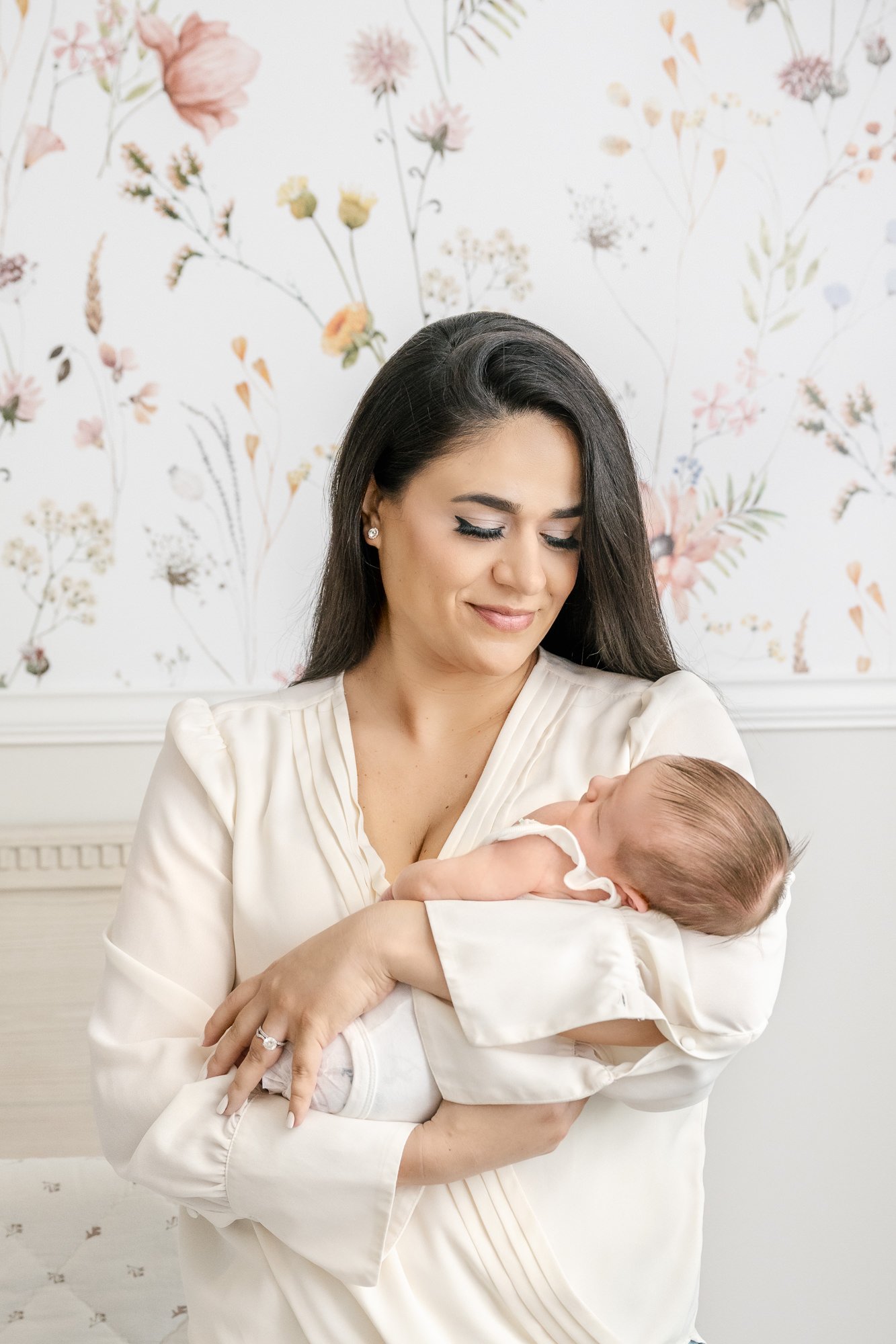  Young mom holds a newborn baby in a luxury nursery. The nursery wallpaper is a timeless floral design. Nicole Hawkins photography captures mom and baby during in-home newborn portrait session. #centralNewJerseyphotographer #inhomeportraits #newbornp