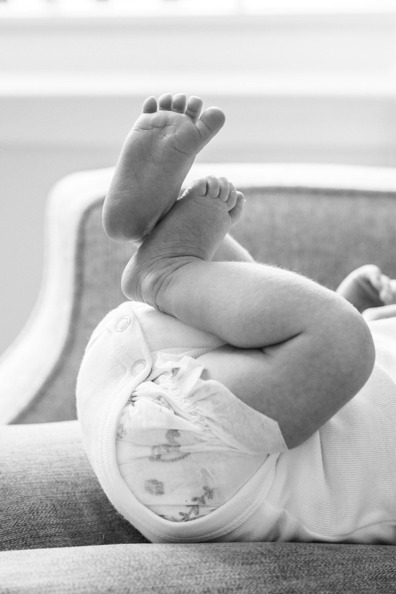  Black and white image of a newborn holding her legs up during a Nicole Hawkins photography session. Cozy nursery used for in-home newborn portrait session. #centralNewJerseyphotographer #inhomeportraits #newbornphotoshoot #NewJerseyPhotographers 