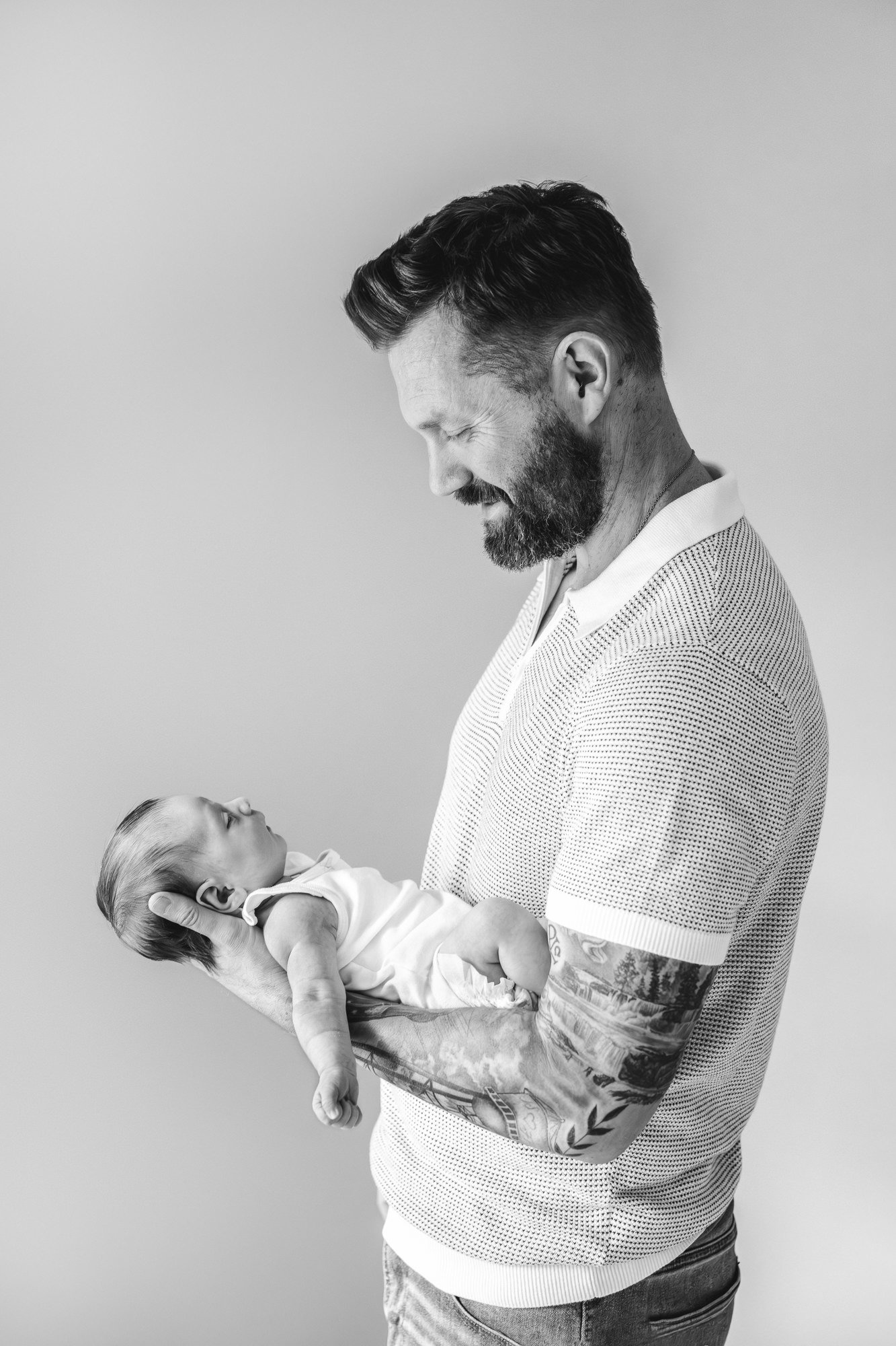  Black and white photo of a dad with his newborn daughter in North Central New Jersey captured by Nicole Hawkins Photography. Dad holds daughter on forearms, showcasing his sleeve of tattoos.&nbsp; #centralNewJerseyphotographer #inhomeportraits #newb