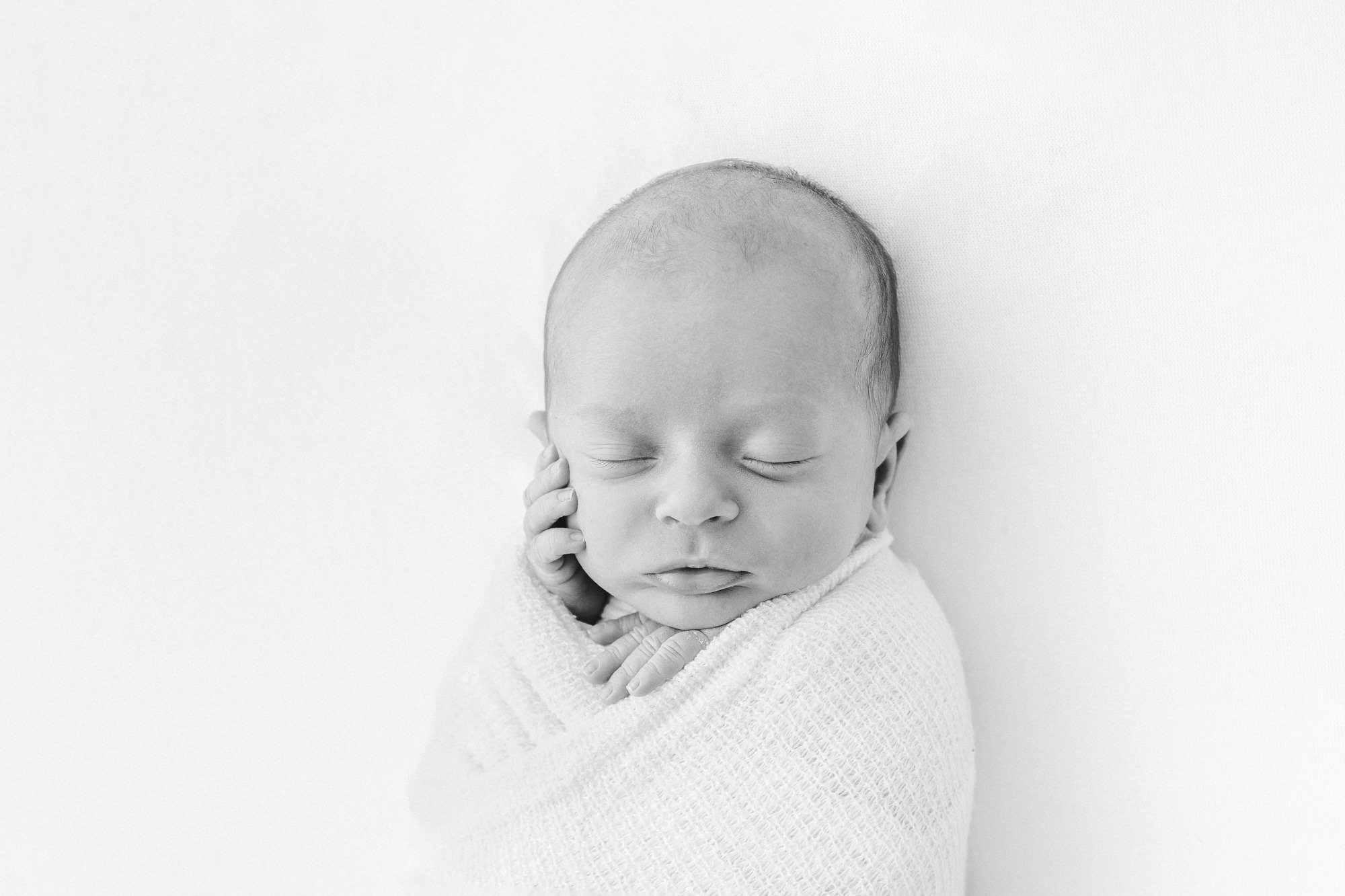  Captivating studio portrait of a newborn baby in black and white, showcasing the baby's peaceful pose with hands near their face captured by Nicole Hawkins photography. #NicoleHawkinsphotography #newbornportraits #NewJerseynewbornphotographer #NewJe