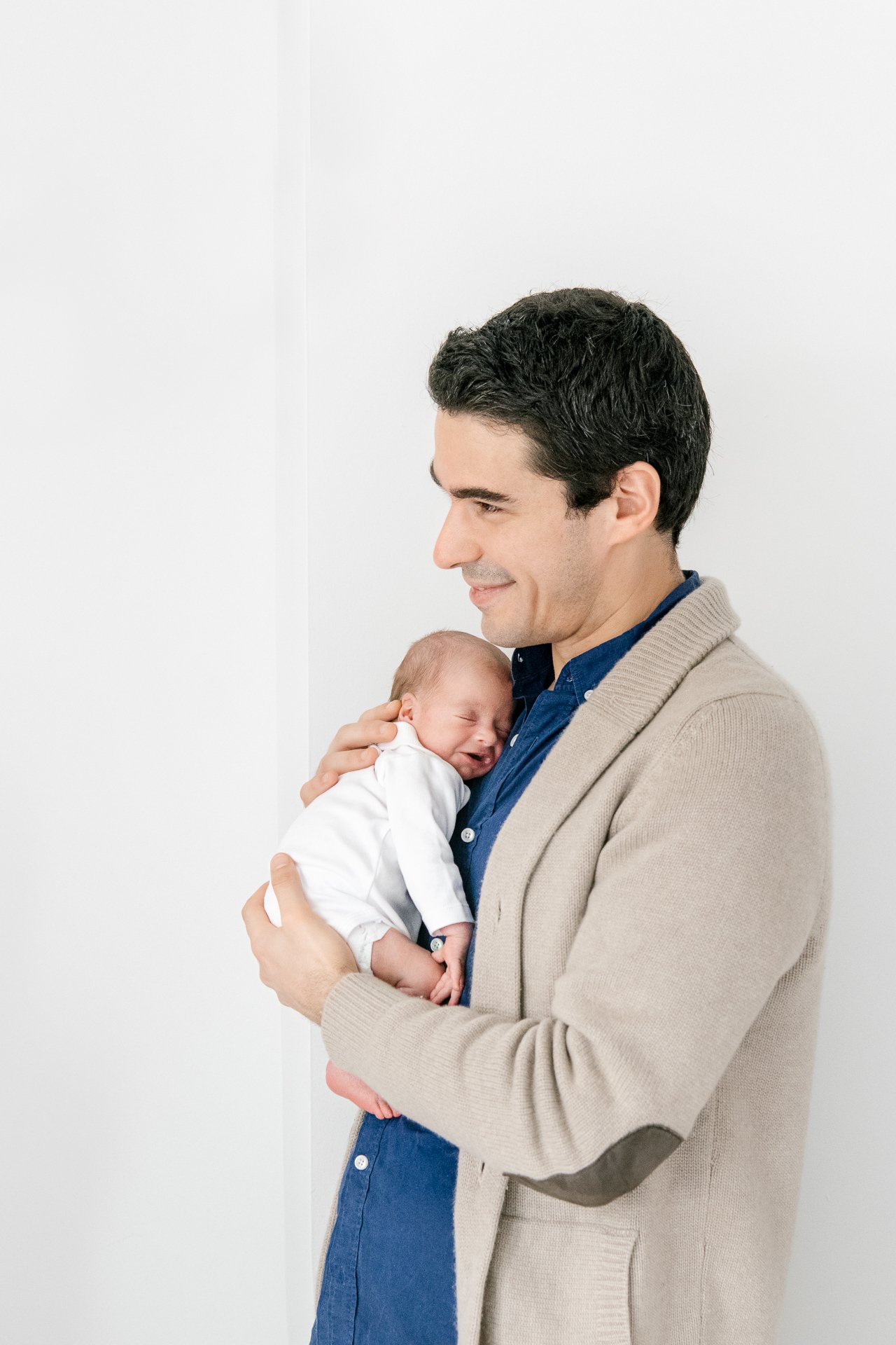  Handsome dad holds his newborn cradled into his chest during a portrait session with Nicole Hawkins Photography, a newborn photographer located in New Jersey.&nbsp; #twinnewbornsessions #NicoleHawkinsphotography #newbornportraits #newbornstudioshoot