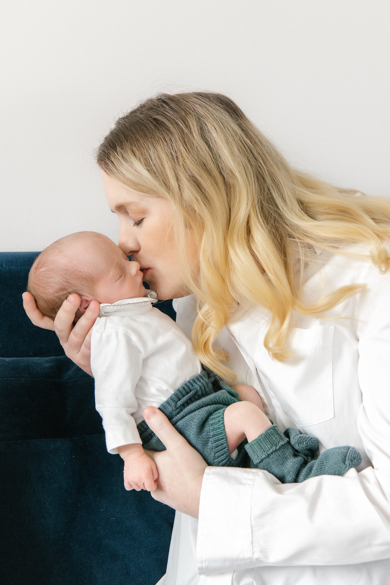  The cutest mom holds one of her newborn babies close as she tenderly places a kiss on the baby’s forehead. Mom dresses in neutral colors to create a timeless image with her baby. Nicole Hawkins photography captures this sweet moment. #twinnewbornses