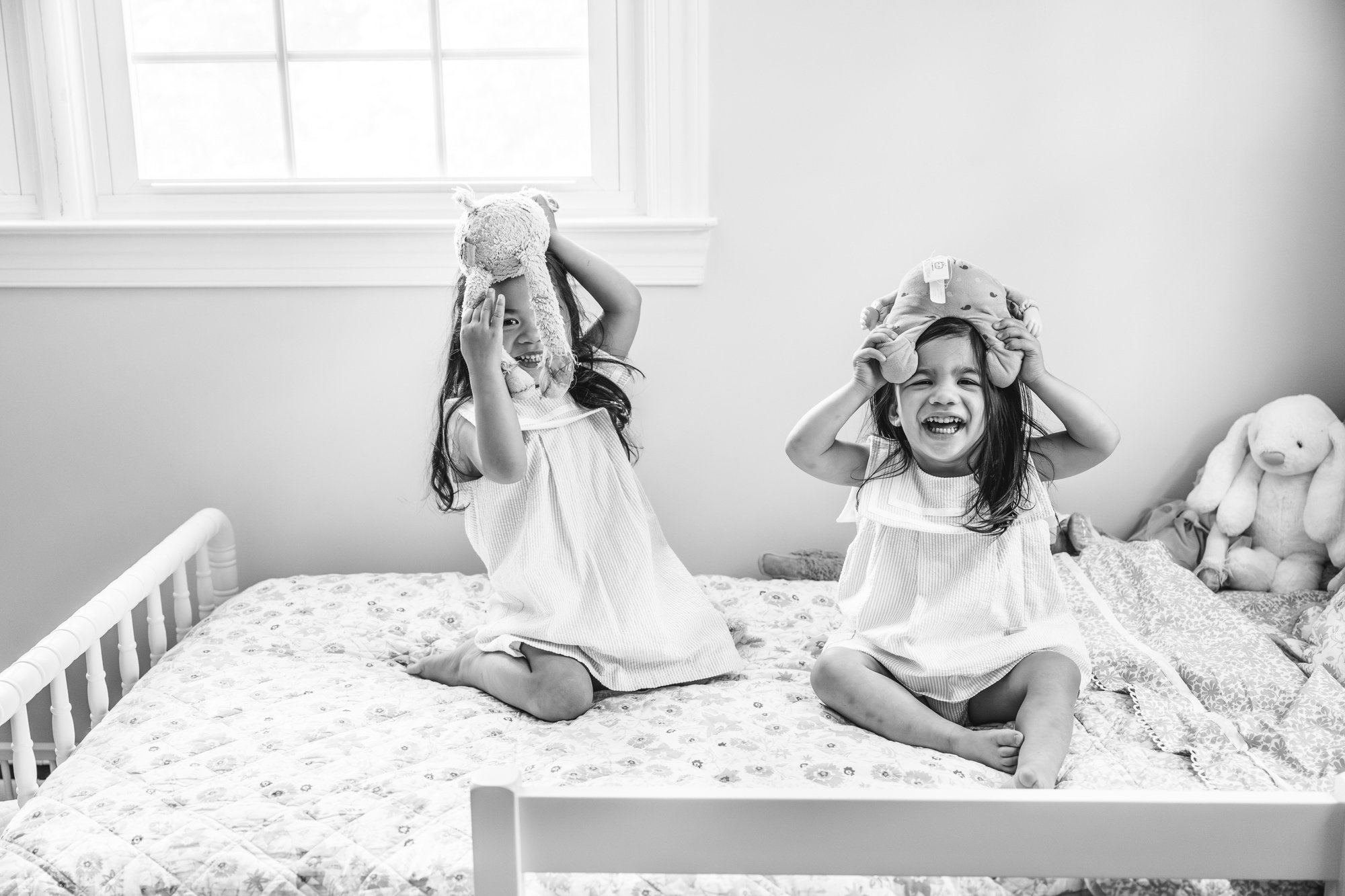  Black and white photo of two young sisters playing and being silly on one of their beds in their bedroom. #newyorkcityphotographer #familyportraits #newbornportraitsession #inhomephotography #familyoffive #familyposeinspo #newjerseyfamilyphotographe