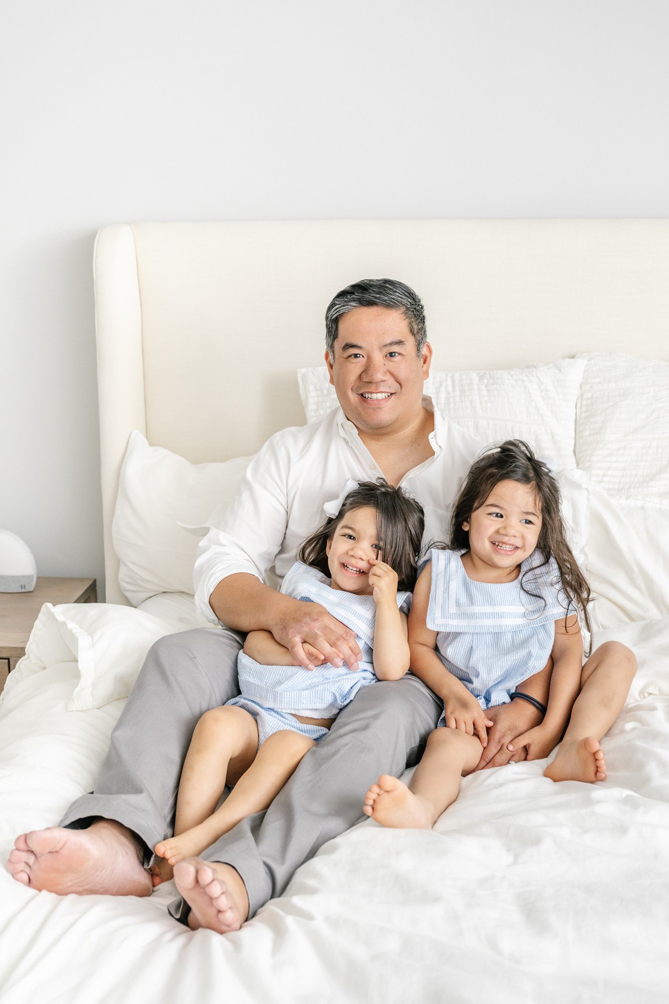  Cute pose idea of a father cuddling up with his two young daughters on the queen bed in their New Jersey home. #newyorkcityphotographer #familyportraits #newbornportraitsession #inhomephotography #familyoffive #familyposeinspo #newjerseyfamilyphotog