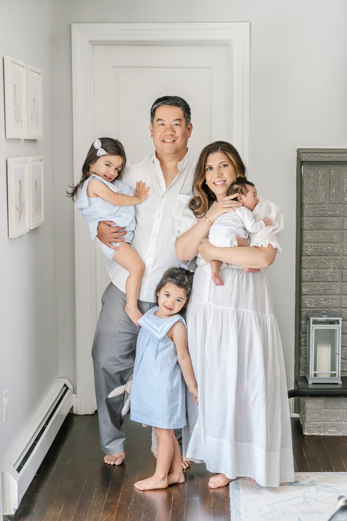  Family with three daughters standing beside their parents together in their home for their in-home newborn portrait session. #newyorkcityphotographer #familyportraits #newbornportraitsession #inhomephotography #familyoffive #familyposeinspo #newjers