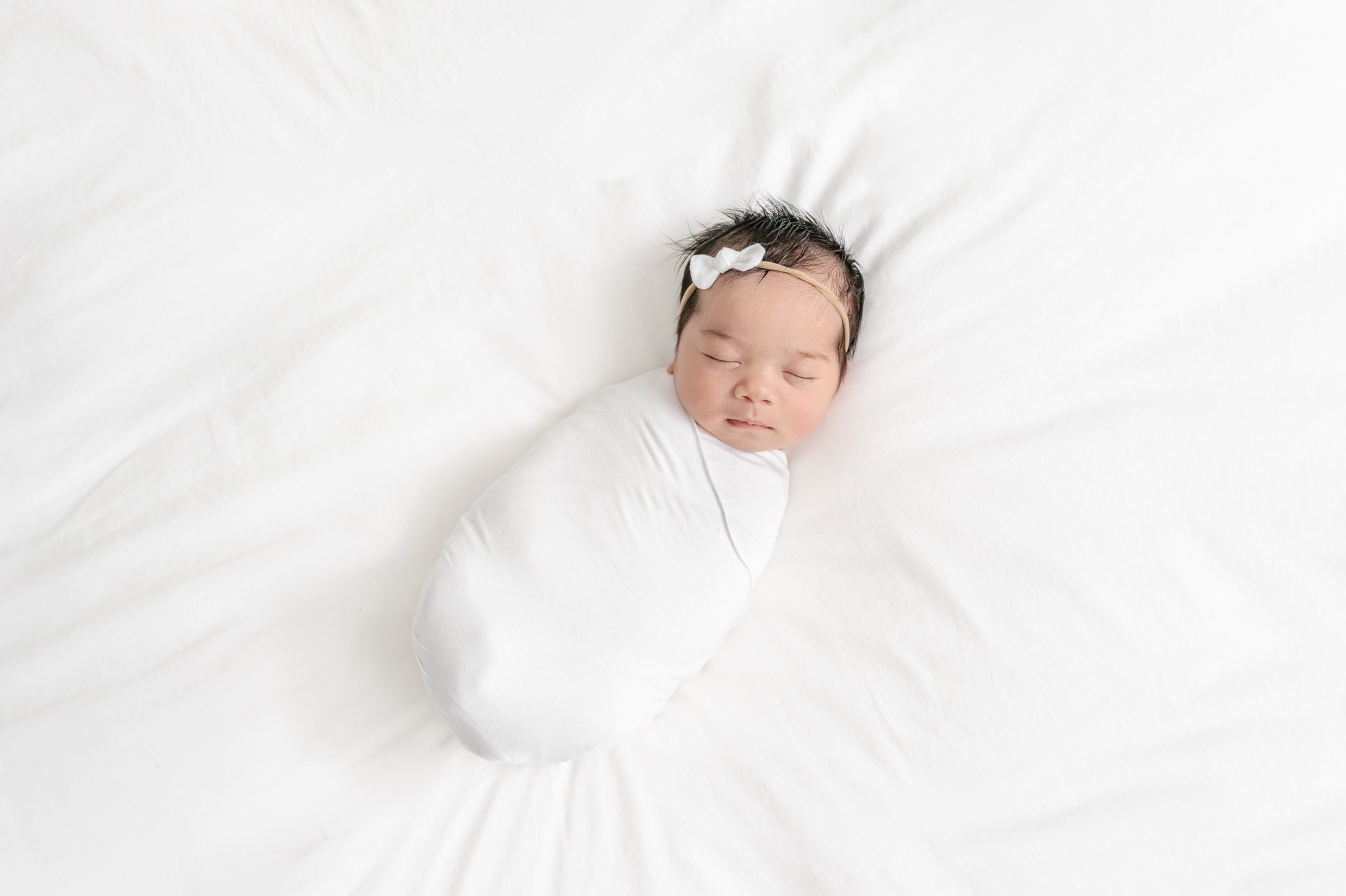  Sweet photograph of a newborn baby girl laying on a bed swaddled in a white gauzy blanket for her in-home newborn session. #newyorkcityphotographer #familyportraits #newbornportraitsession #inhomephotography #familyoffive #familyposeinspo #newjersey