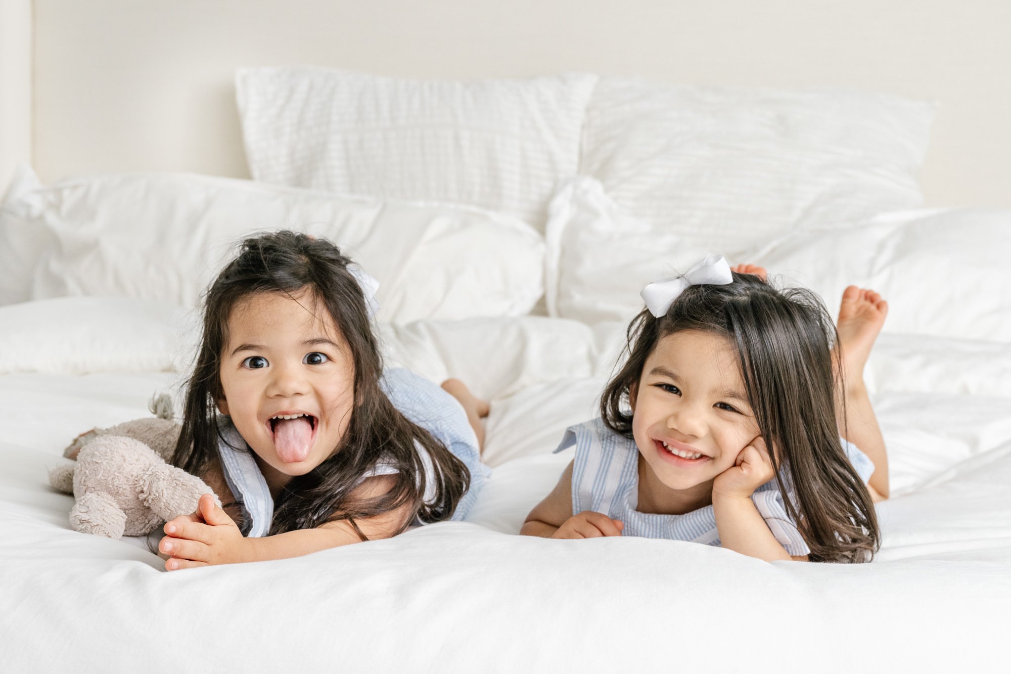  A fun photo of two sisters laying on mom and dad’s bed making silly faces while laughing together during their family portrait session. #newyorkcityphotographer #familyportraits #newbornportraitsession #inhomephotography #familyoffive #familyposeins