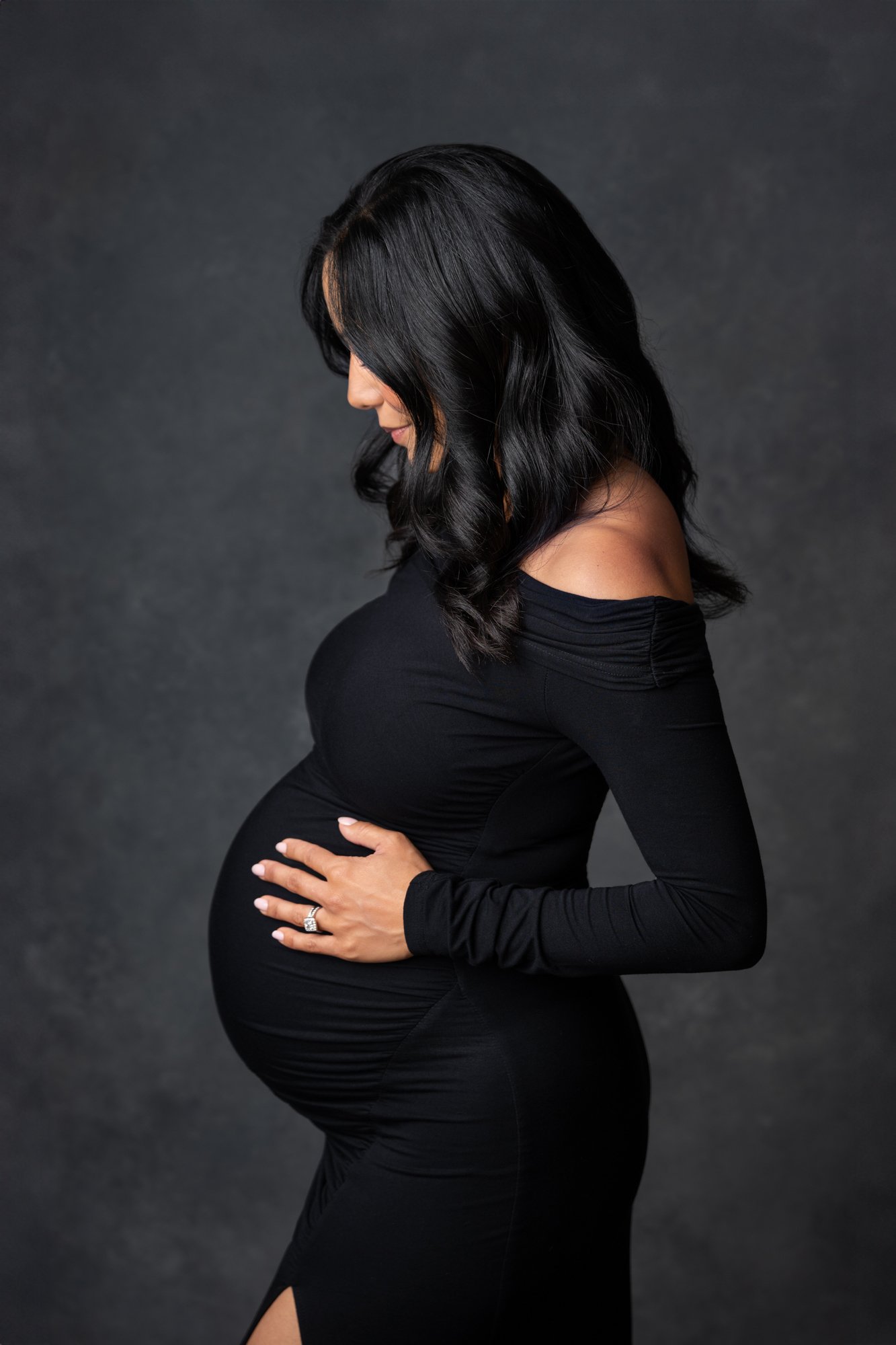  Stunning mother wears a fitted black dress to show off her baby bump in her studio maternity photography session in New Jersey. #southorange #newjerseyphotographers #maternitysession #maternityposeinspo #studiophotography #formalmaternitystyle #casu