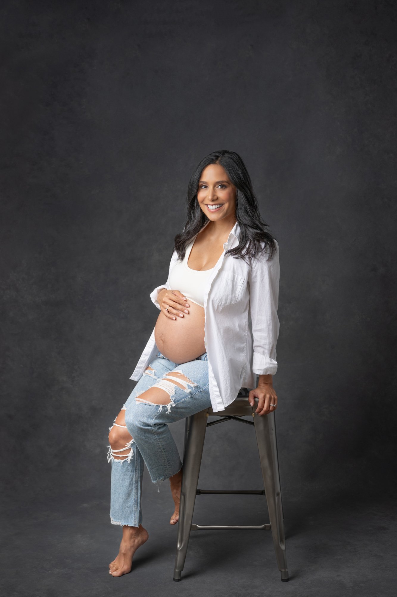  Pregnant mother poses on a metal bar stool during a maternity photography session with Nicole Hawkins Photography. #southorange #newjerseyphotographers #maternitysession #maternityposeinspo #studiophotography #formalmaternitystyle #casualmaternityst