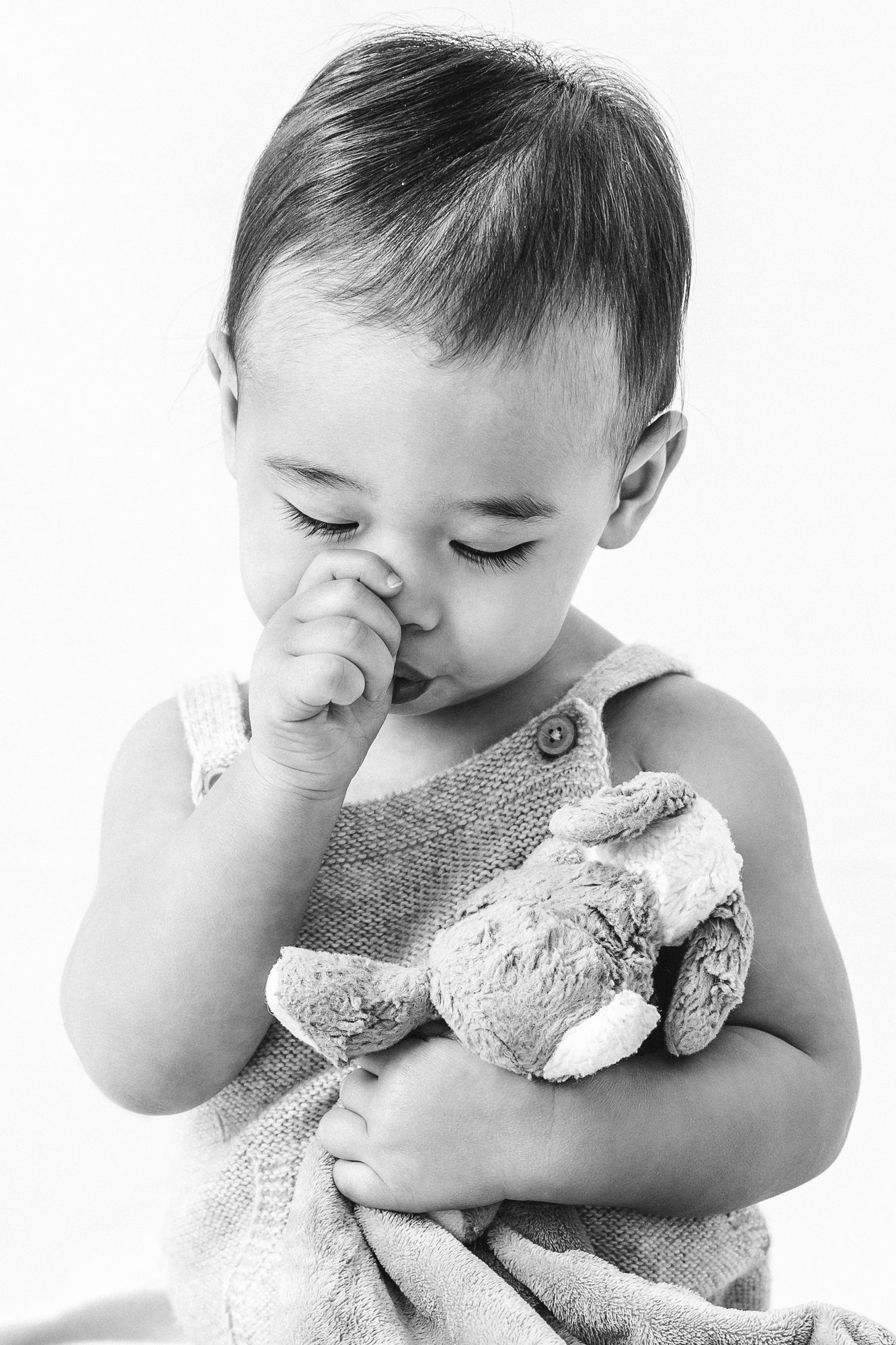   Intimate black and white family photoshoot with child holding teddy bear and sucking his thumb taken by Nicole Hawkins, Northern New Jersey Family Photographer. Toddler poses for family photos #EssexCountyFamilyPhotographer #BergenCountyFamilyPhoto