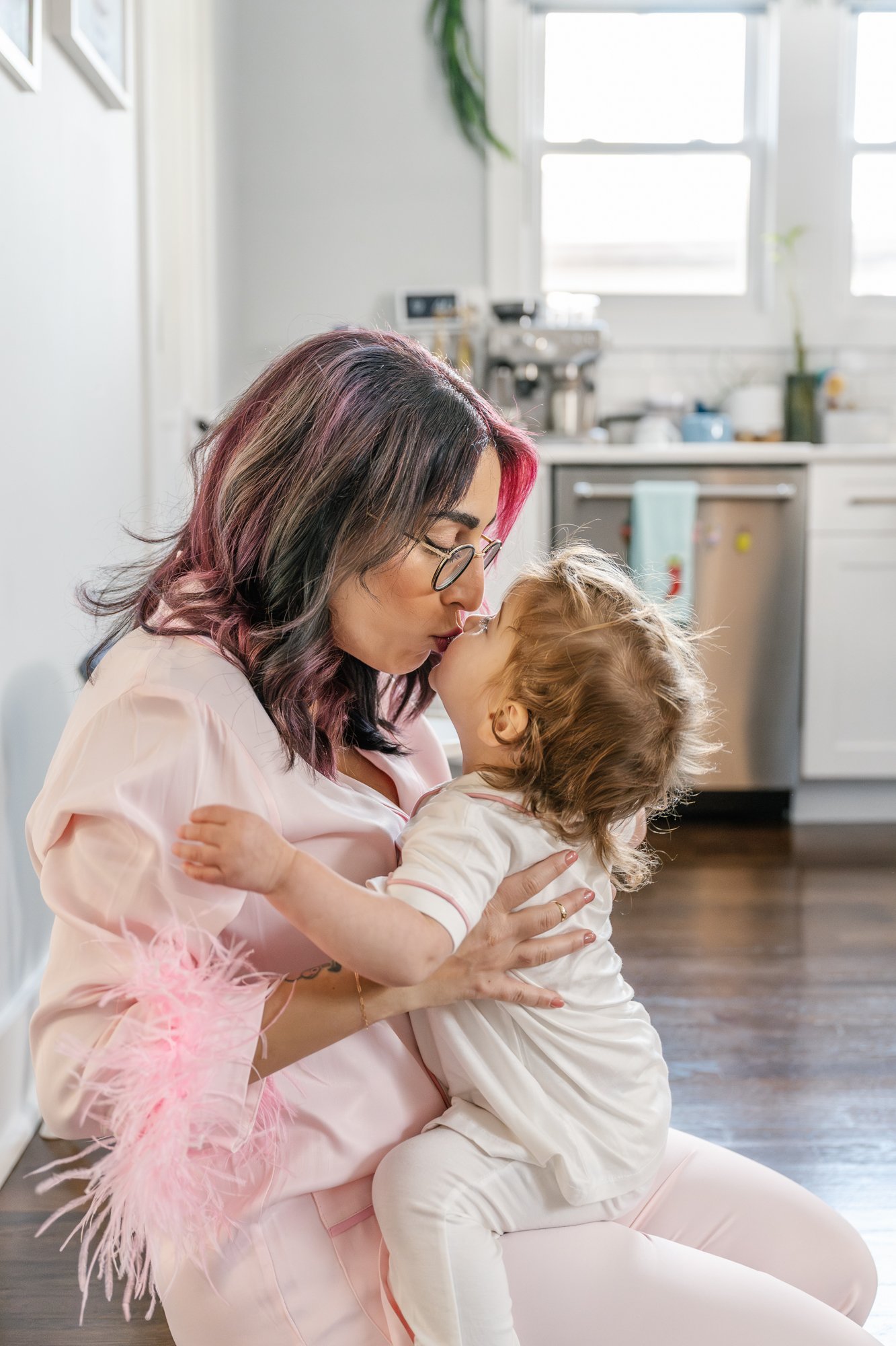   Mom kissing daughter sitting on kitchen floor during casual at home family photoshoot wearing pajamas. Casual family photo inspiration#EssexCountyFamilyPhotographer #MorrisCountyFamilyPhotographer #NorthernNewJerseyFamilyPhotographer #ManhattanFami