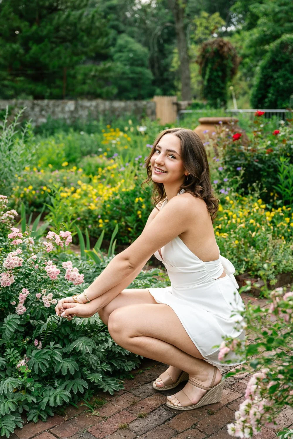 Smiling senior girl in a white dress surrounded by flowers at Cross Estate Gardens