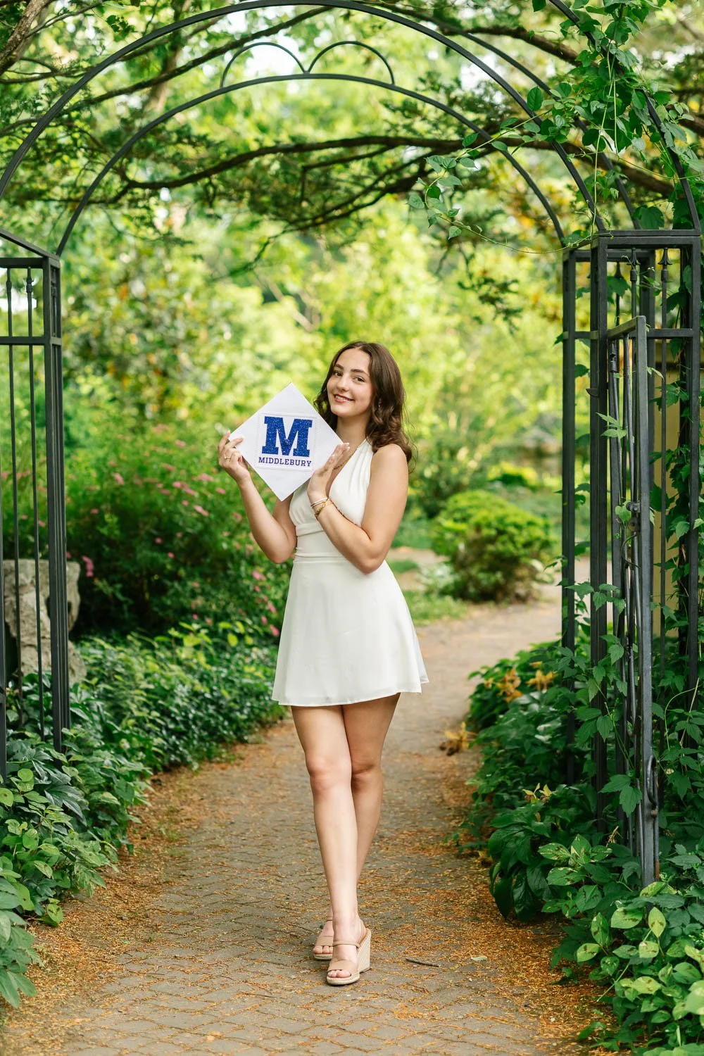 Full length senior portrait of a graduating Maplewood senior holding her graduation cap decorated for Middlebury College