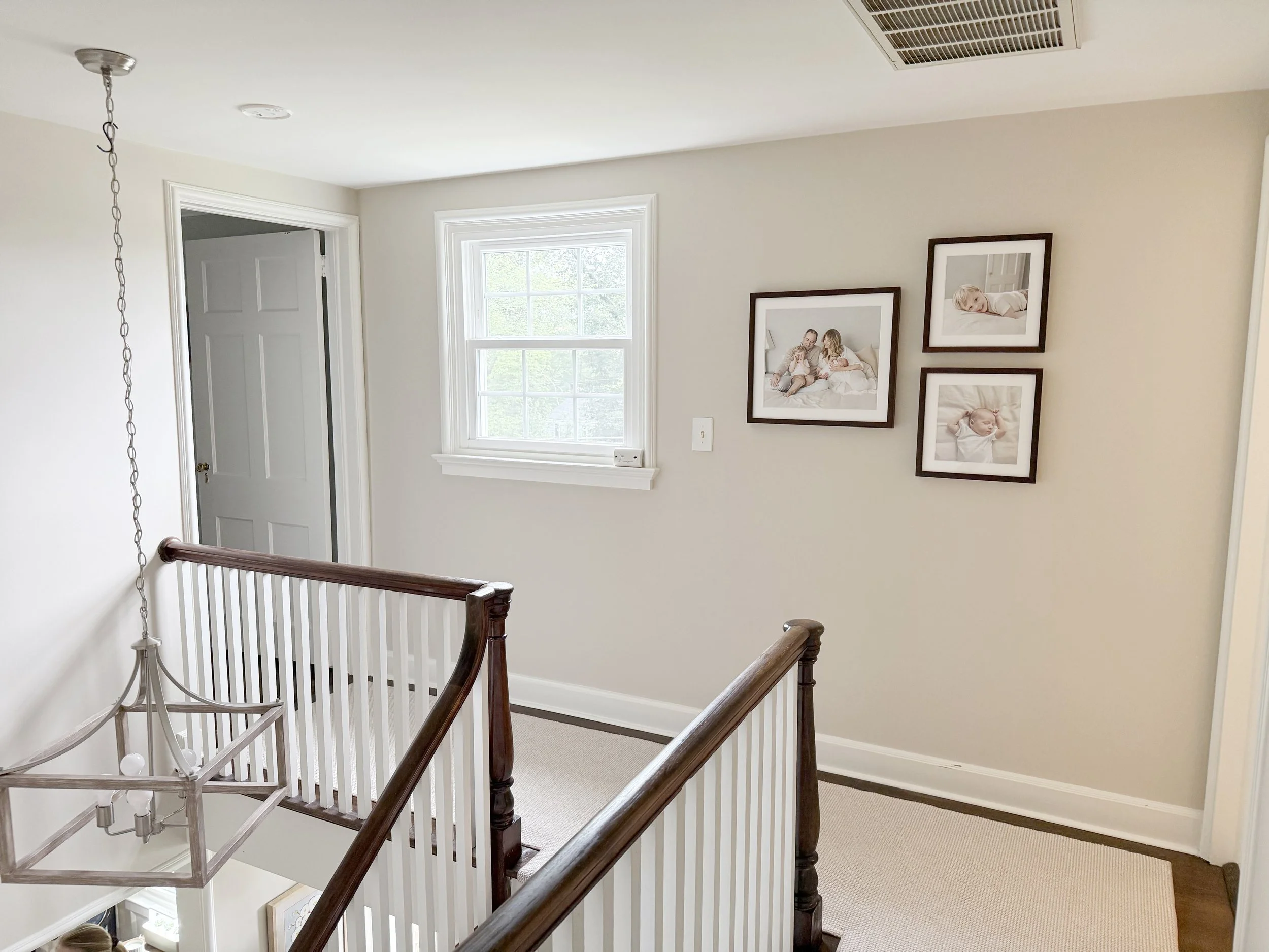 A hallway on the upper floor of a Morris County with framed family and newborn photos on the beige wall.