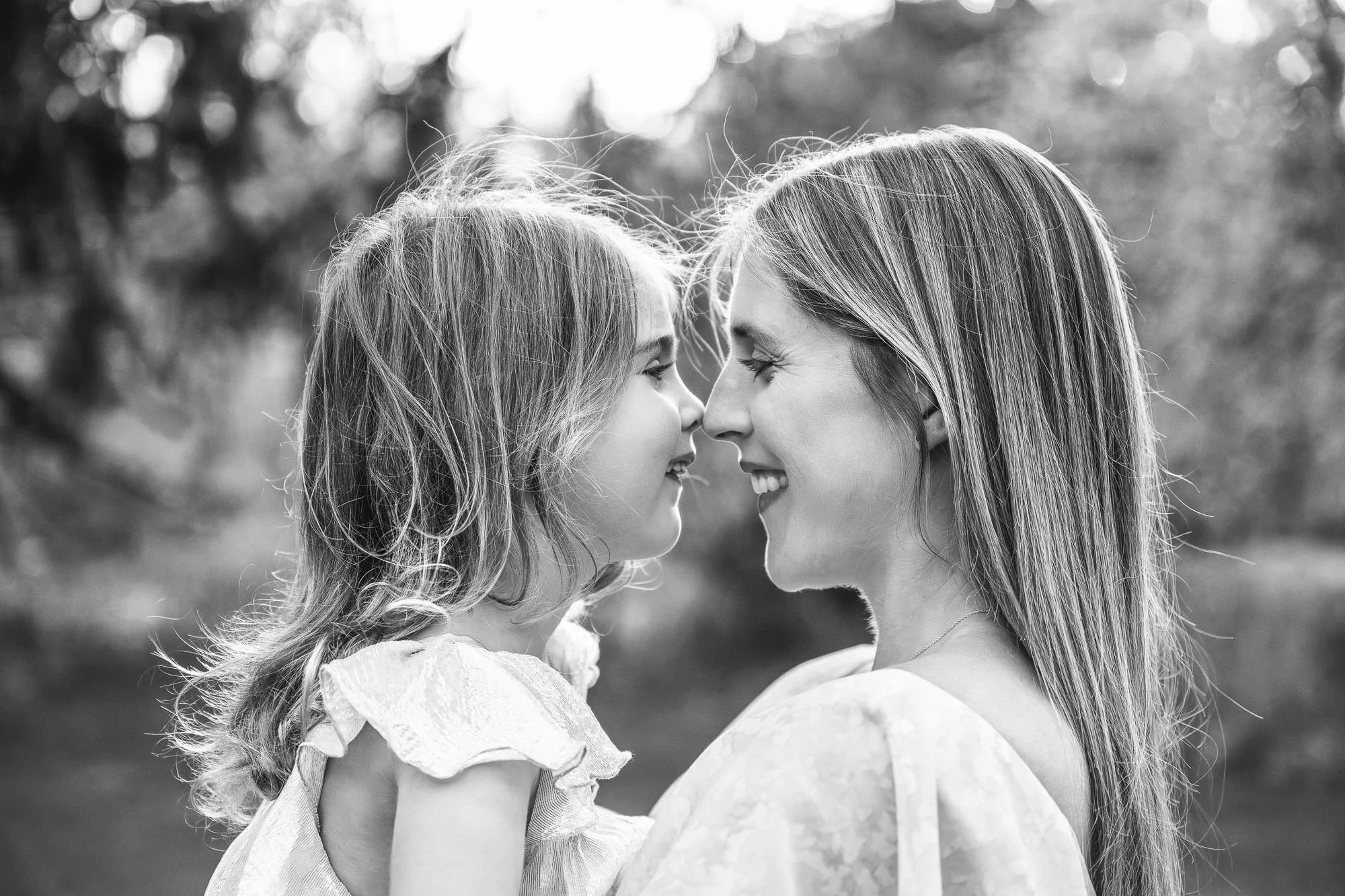 Bright black and white profile photo of mother and daughter smiling and touching noses in Old Short Hills NJ Park