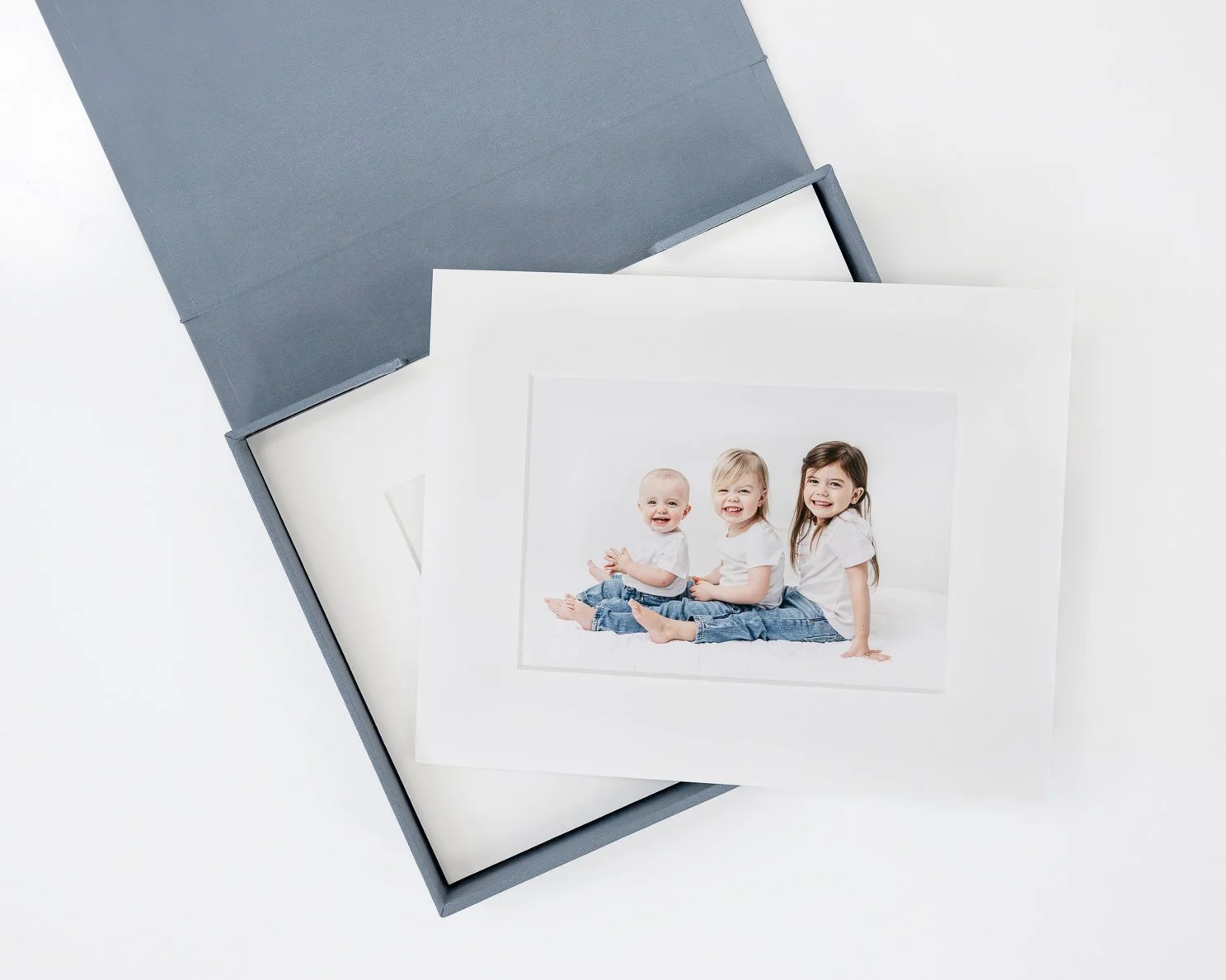 Classic portrait of three young sisters wearing white t-shirts and blue jeans children sitting on white bed in NJ studio.