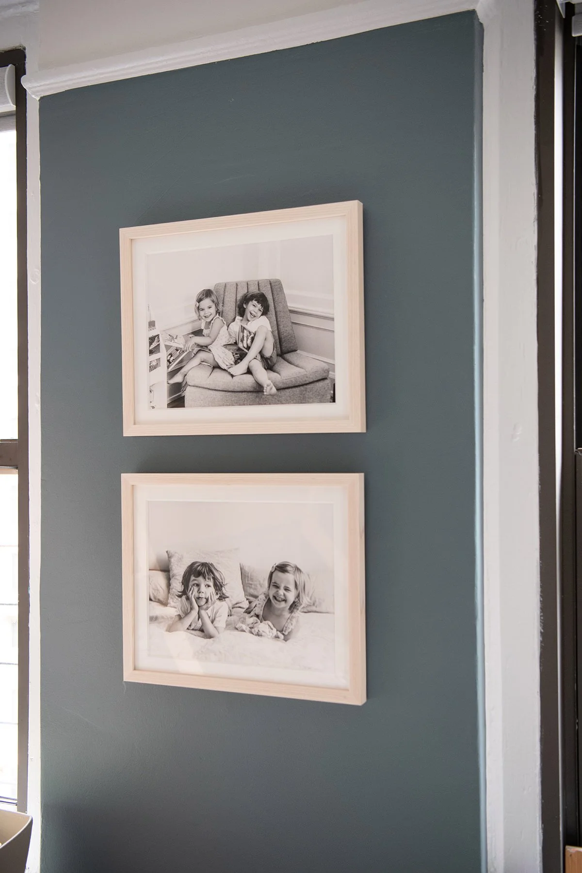 Two framed black-and-white sibling photographs of young children are hung on a gray wall at home.