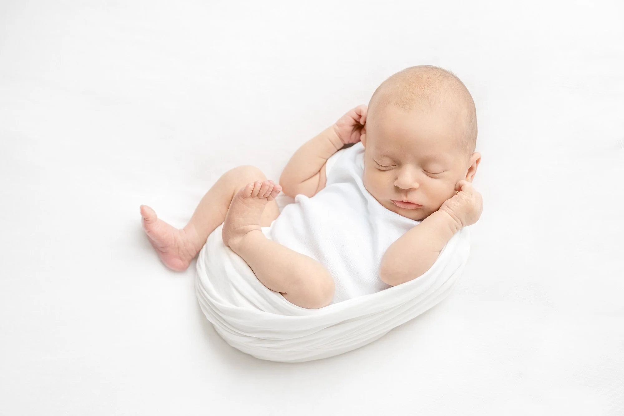 Adorable newborn baby in a white onesie, a bundle of pure innocence and joy captured by Nicole Hawkins photography in a studio in New Jersey.  #NicoleHawkinsphotography #newbornportraits #NewJerseynewbornphotographer #NewJerseyportraits