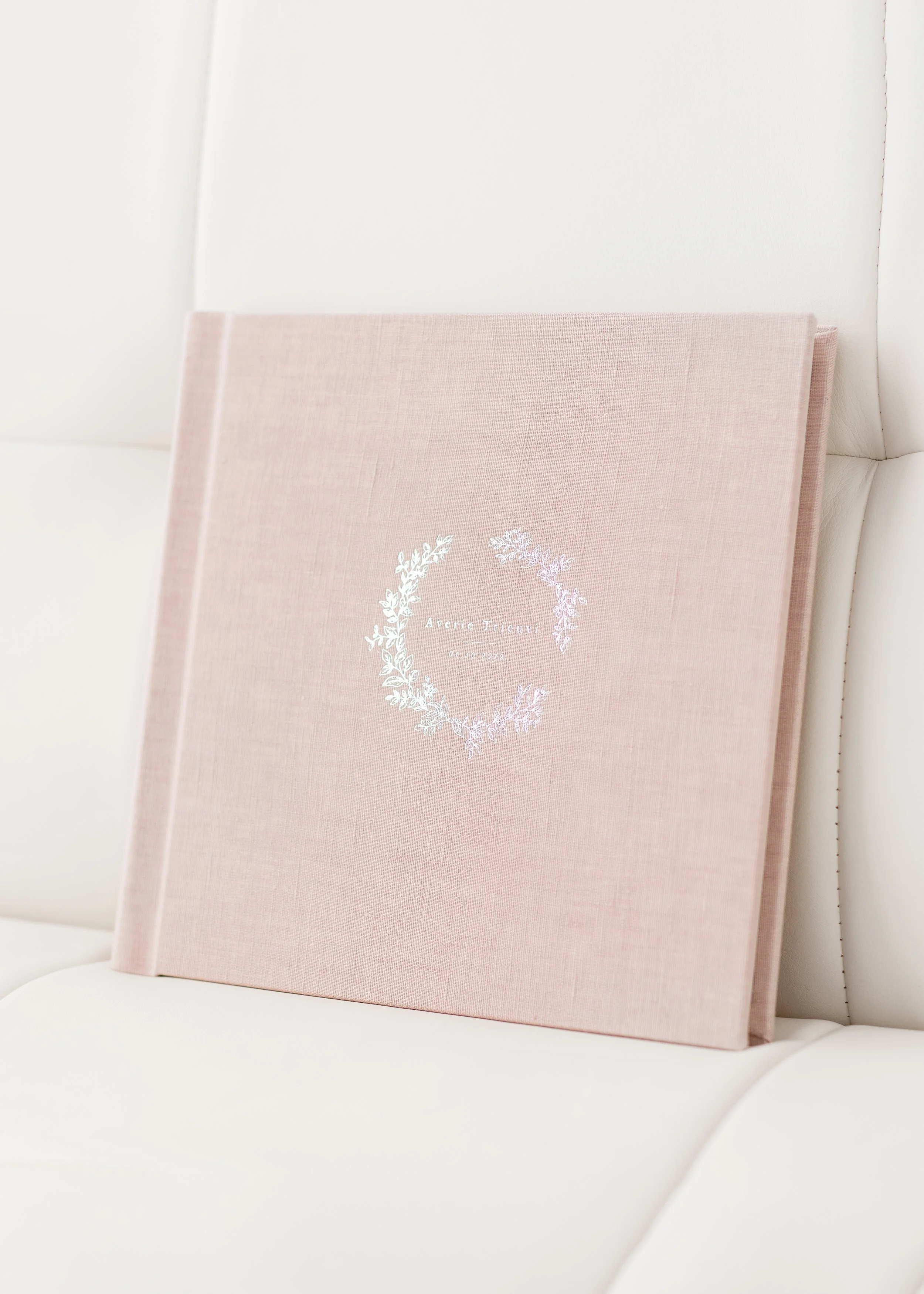A newborn baby album with floral and text design on the cover, resting against a white cushioned couch.